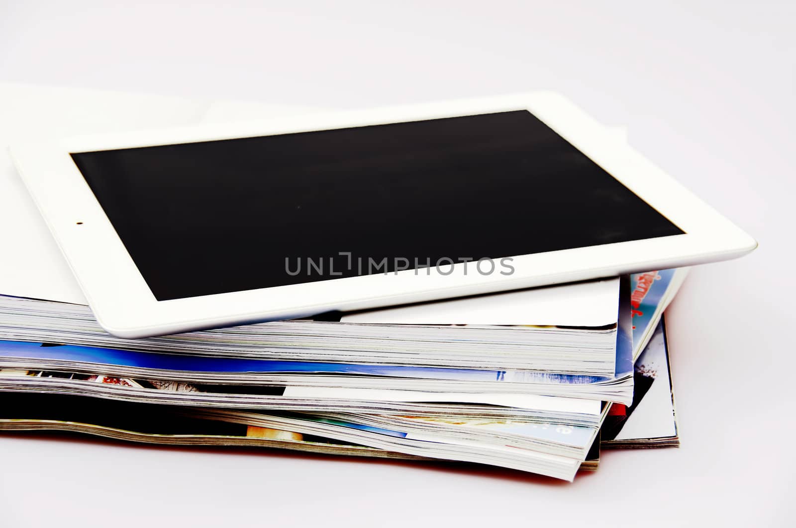 A white tablet on top of a stack of magazines and books