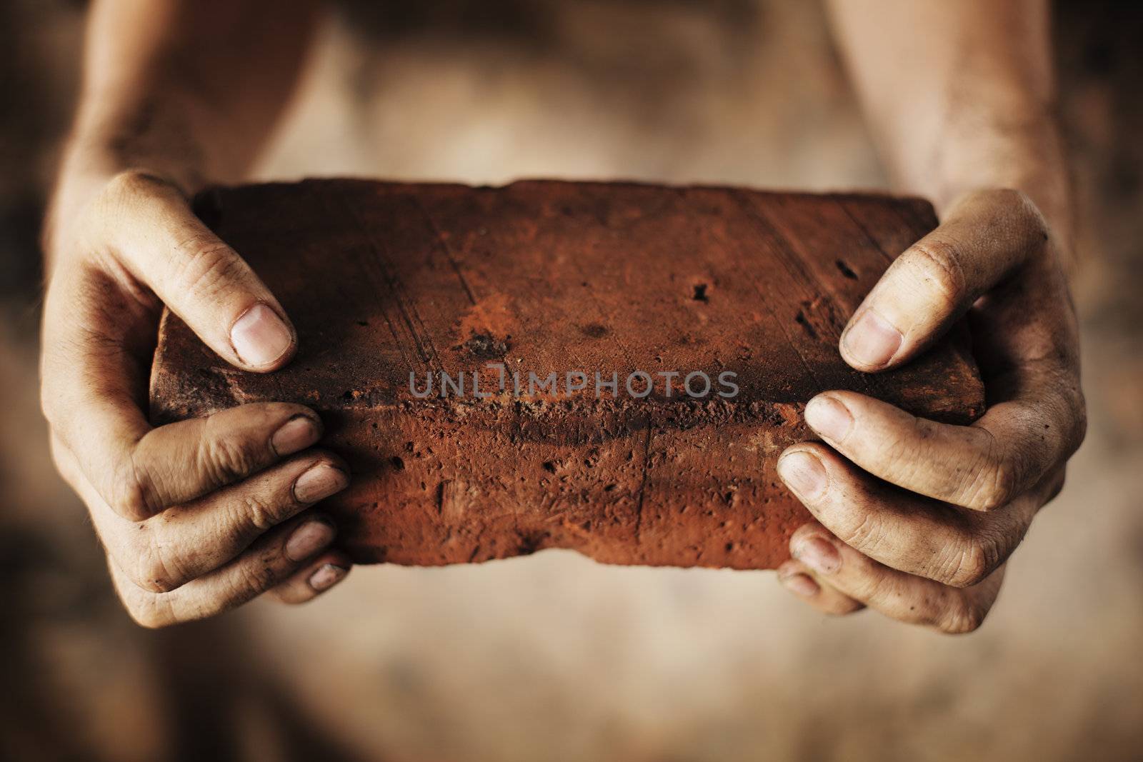 Dirty hands holding an old brick