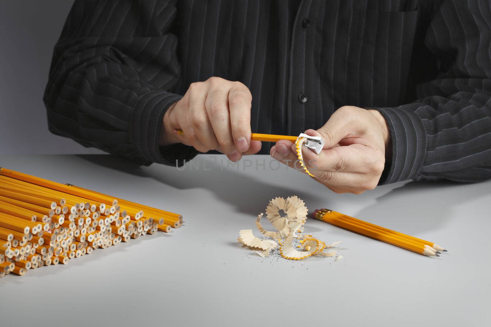 Man sharpening a heap of pencils with a pencil sharpener.