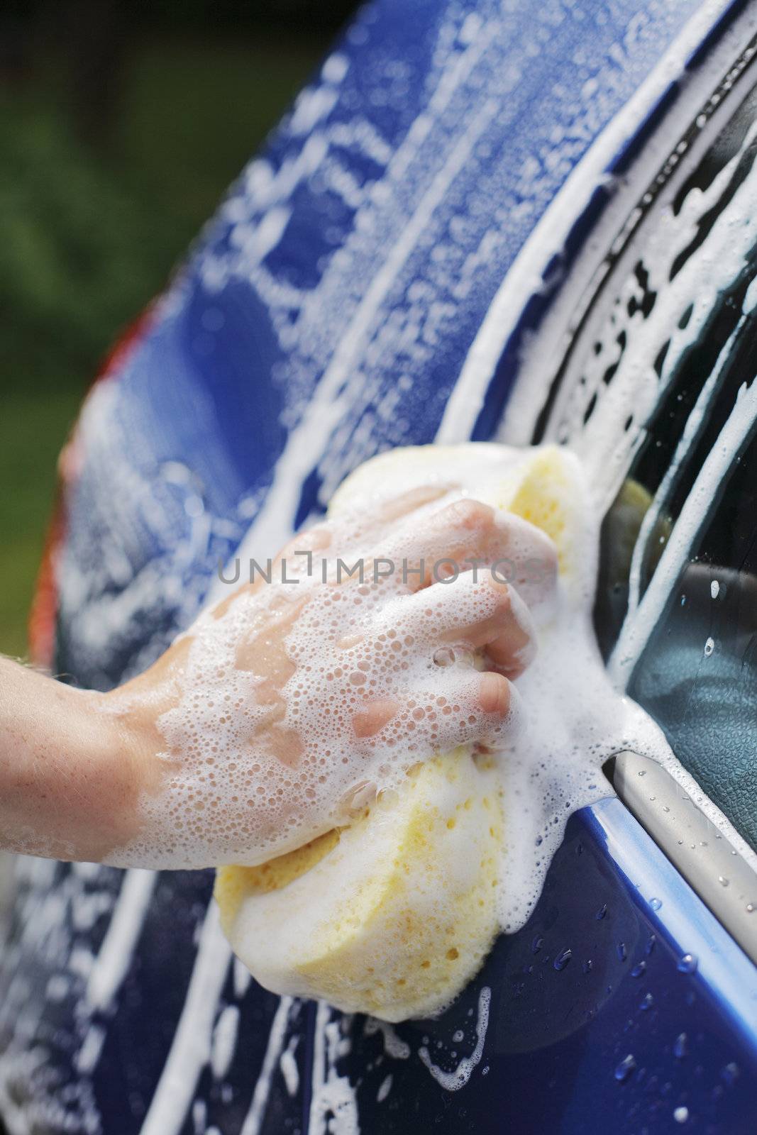 A Hand washing a blue car with a sponge