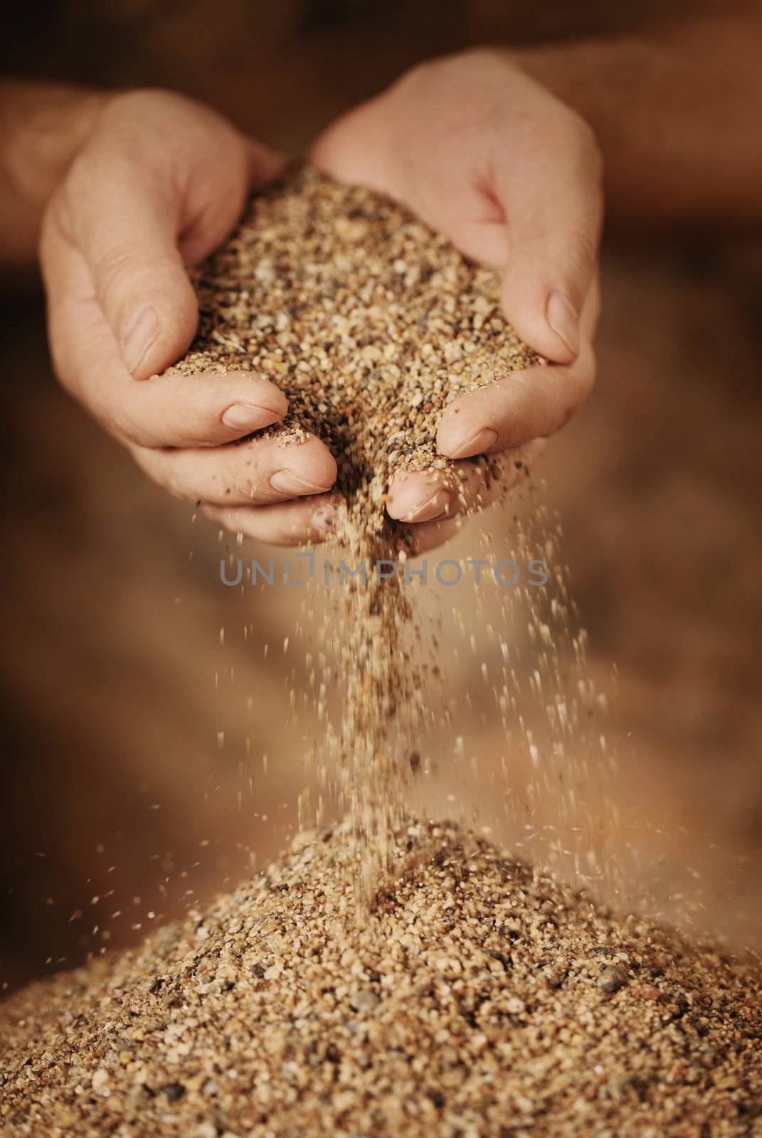 Man adding coarse sand to a heap with his hands. Very shallow depth-of-field and motion blur.