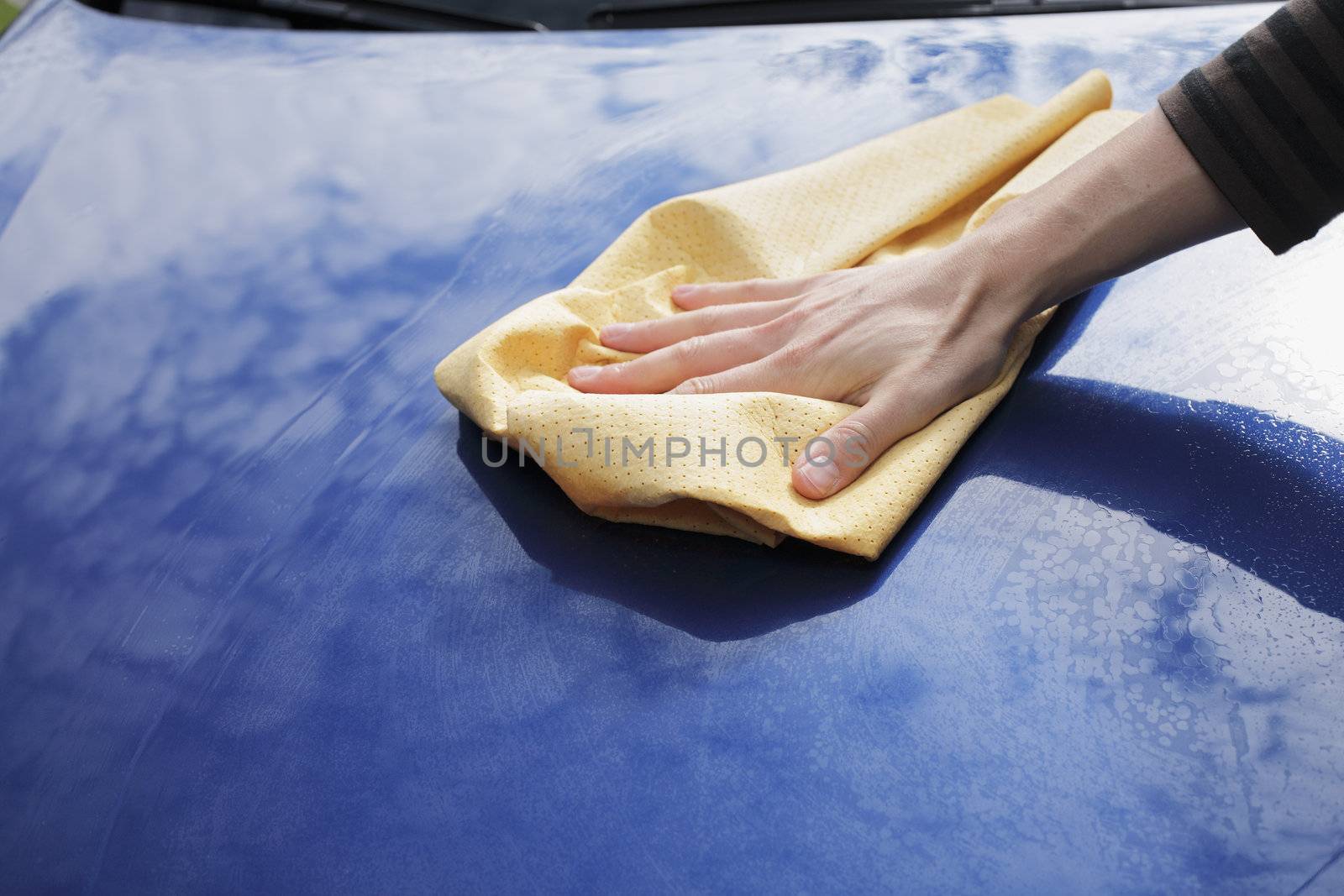 A Hand drying a blue car with a synthetic chamois leather.