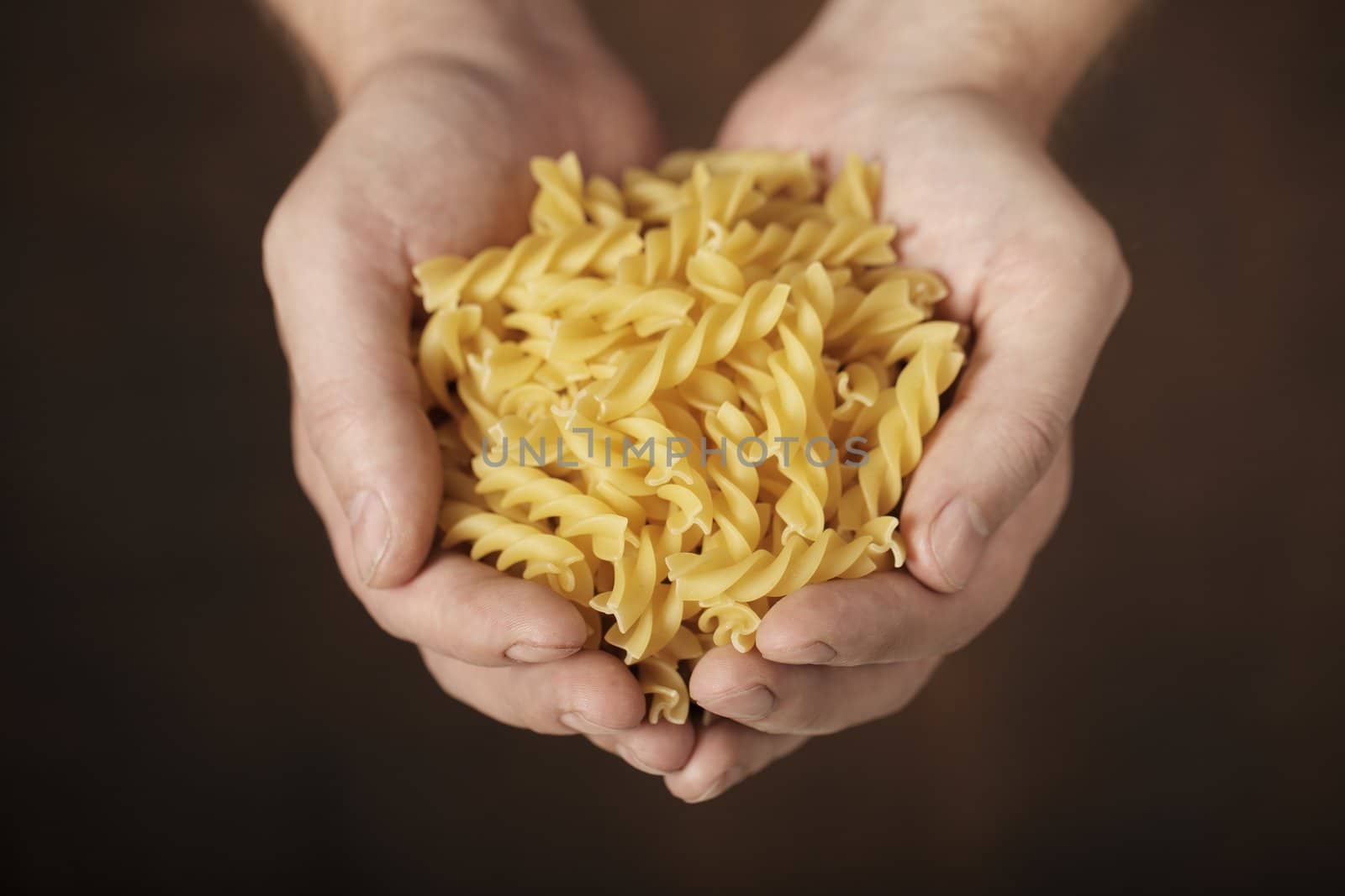 Man holding uncooked fusilli pasta in his hands. Very short depth-of-field.