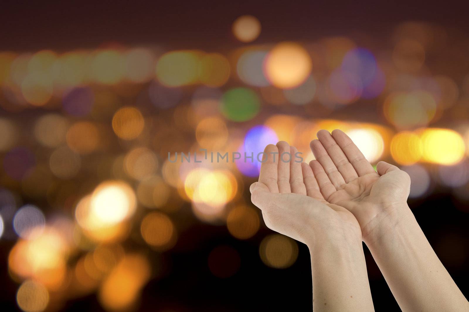 Hopefully beseeching cupped female hands held  against colorful lights background