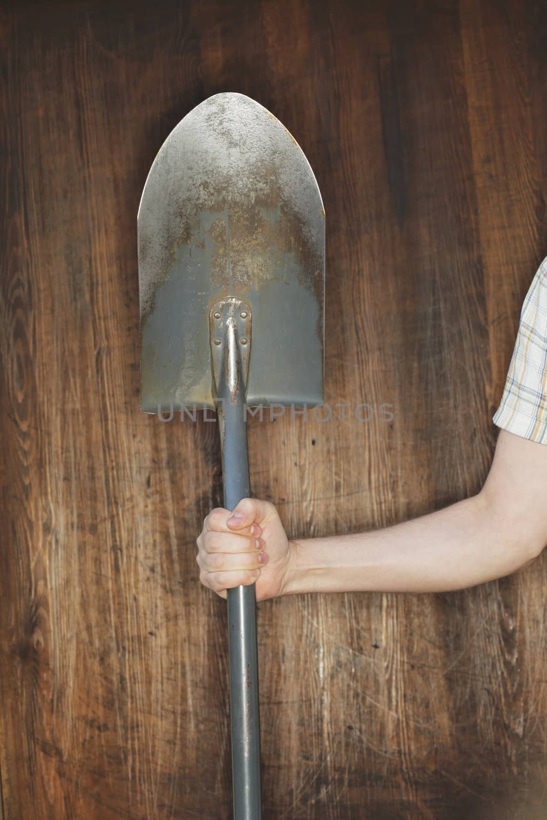 Man holding a spade in front of wooden background.