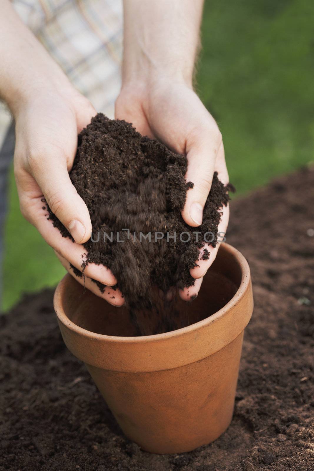 Hands putting soil into a clay flower pot