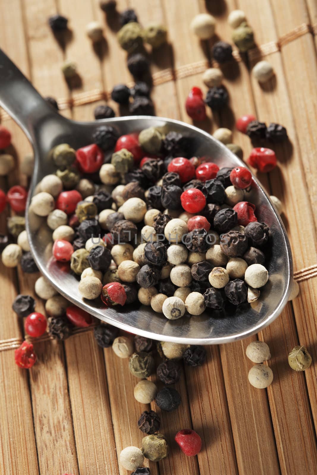 A mix of black, green, red and white peppercorns on a spoon