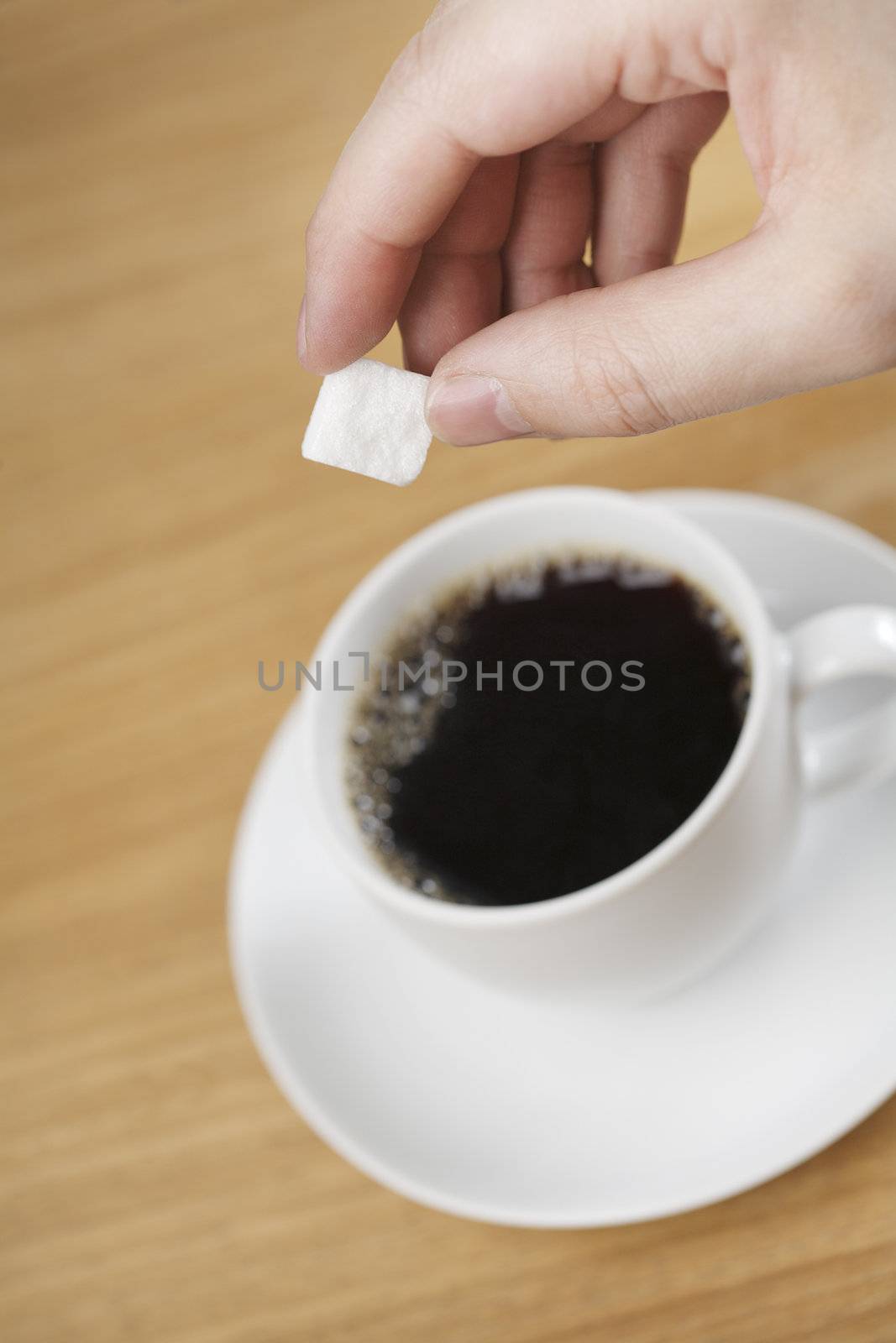 Hand adding sugar to a cup of coffee. Short depth of field.