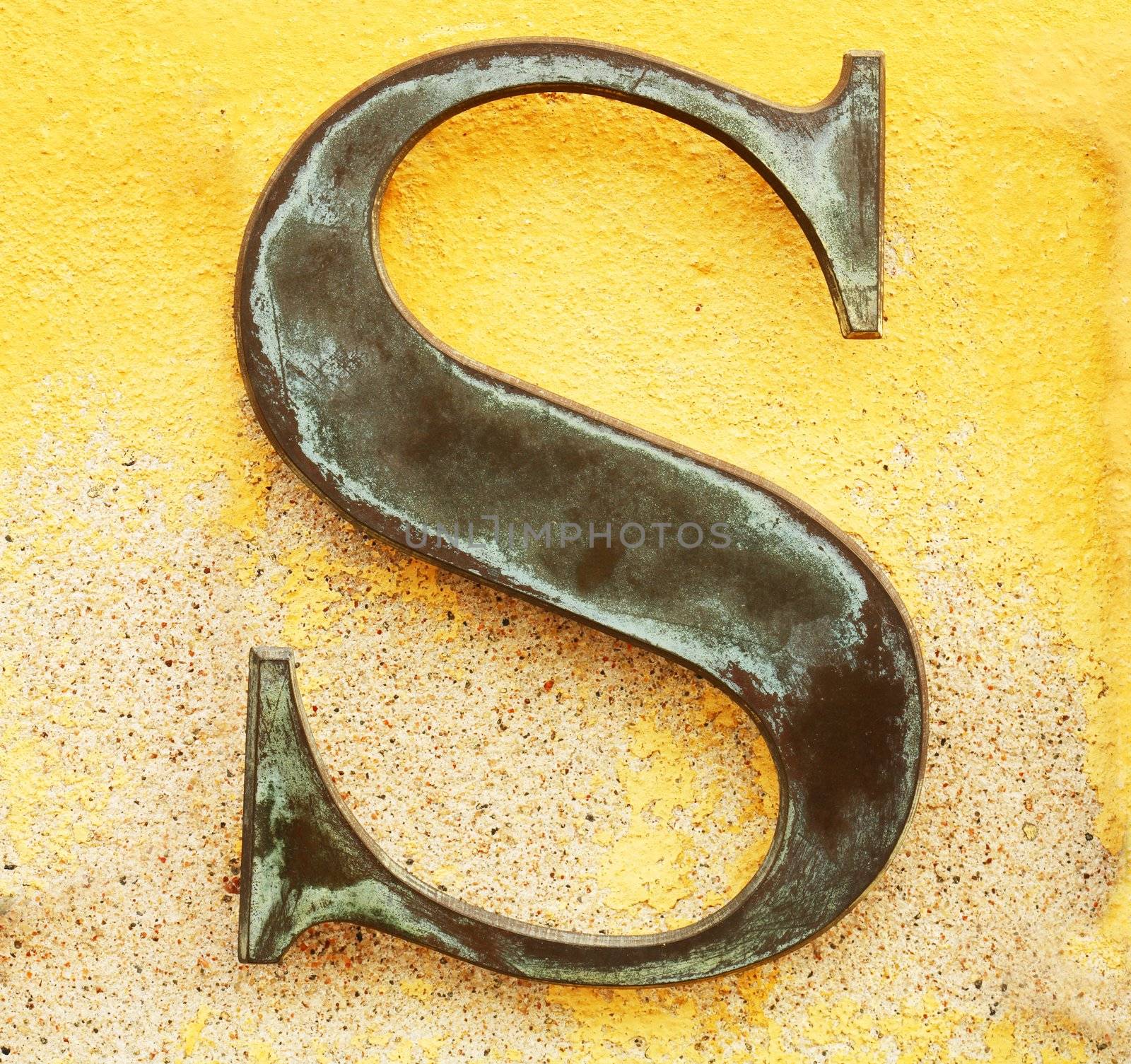 Metallic letter 'S' on yellow wall.