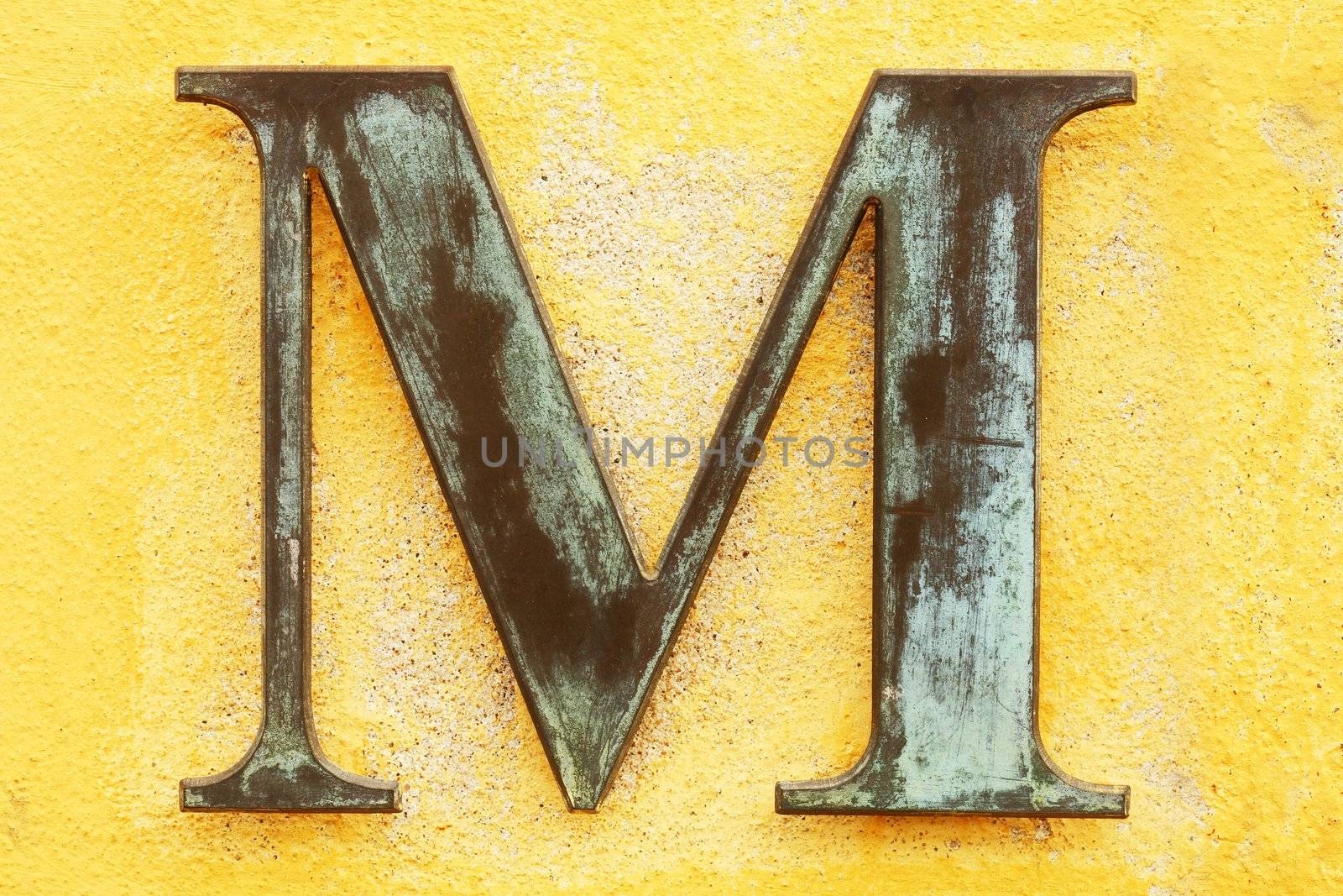 Metallic letter 'M' on yellow wall