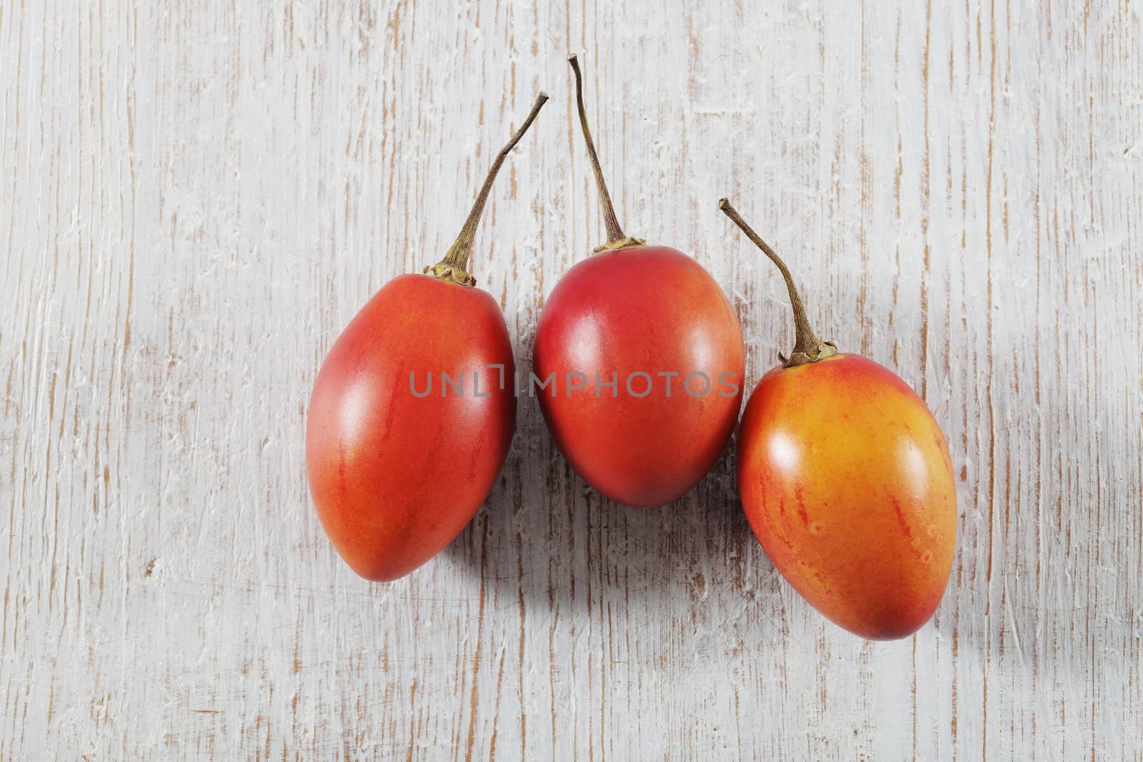 Three Tamarillo fruit (tree tomato) on white wooden background.