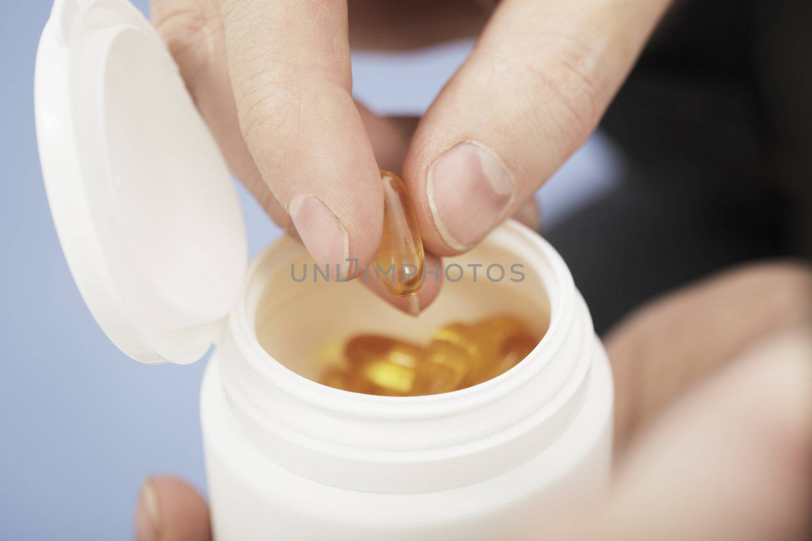 Fingers taking Omega 3 fish oil capsule from a bottle