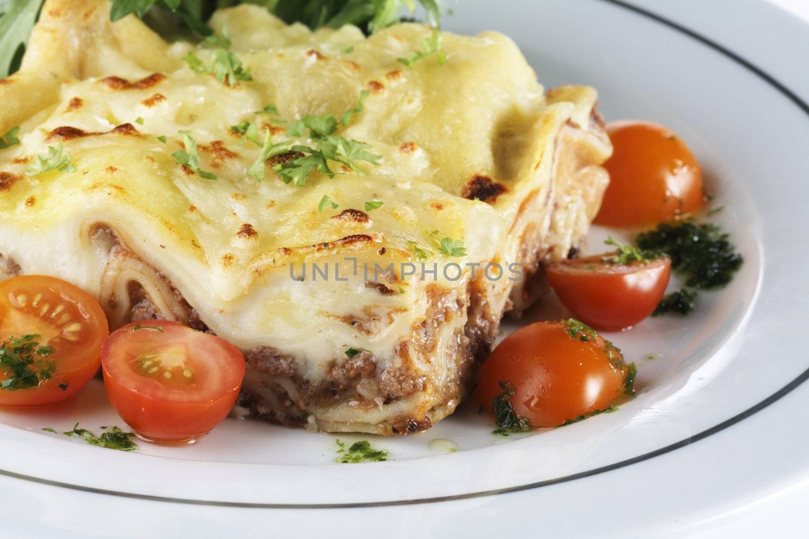 Minced meat lasagna on a plate with some tomatoes