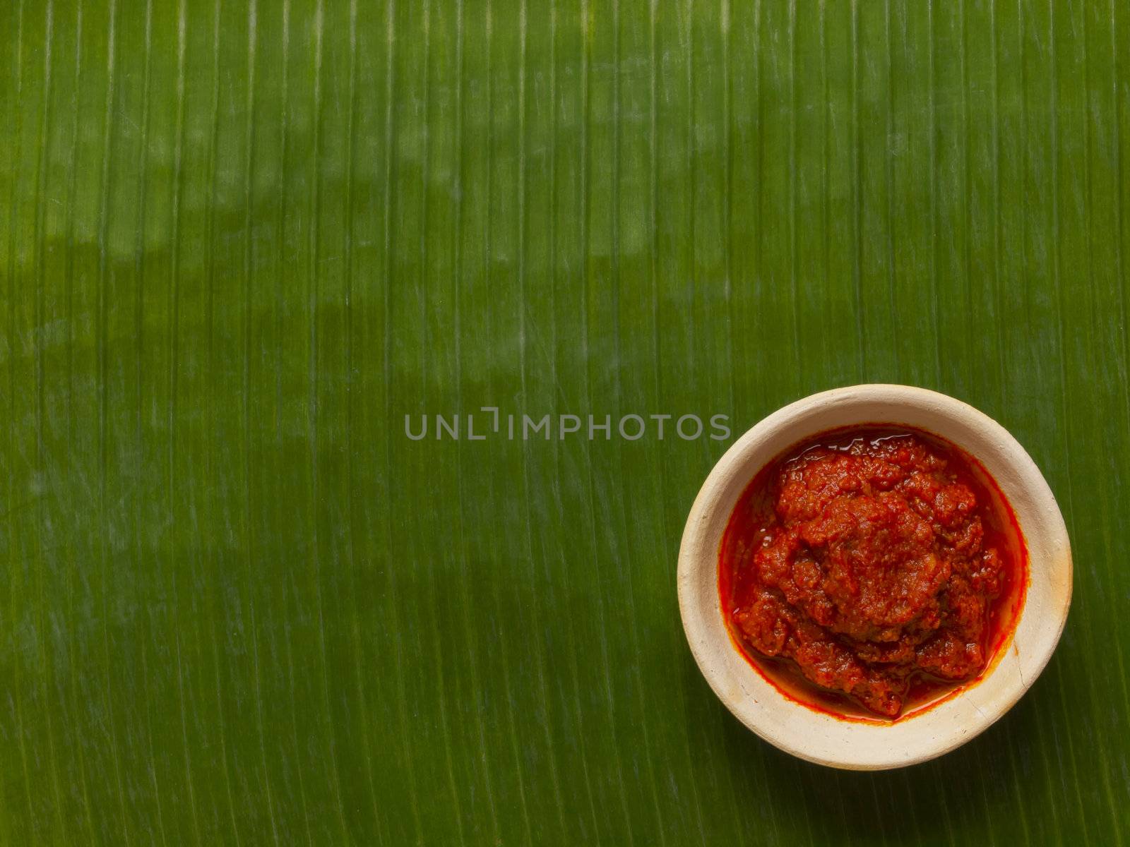 close up of a bowl sambal chili sauce on banana leaf background