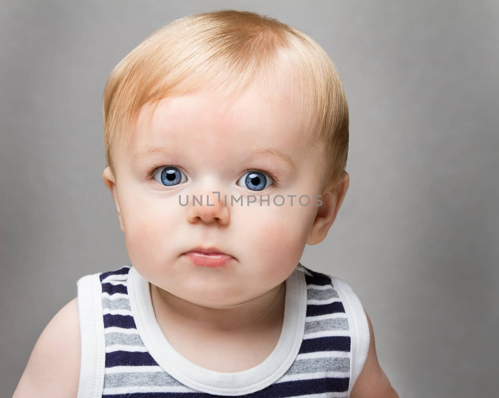 Toddler against a medium to dark grey  background. Very bright eyed and adorable