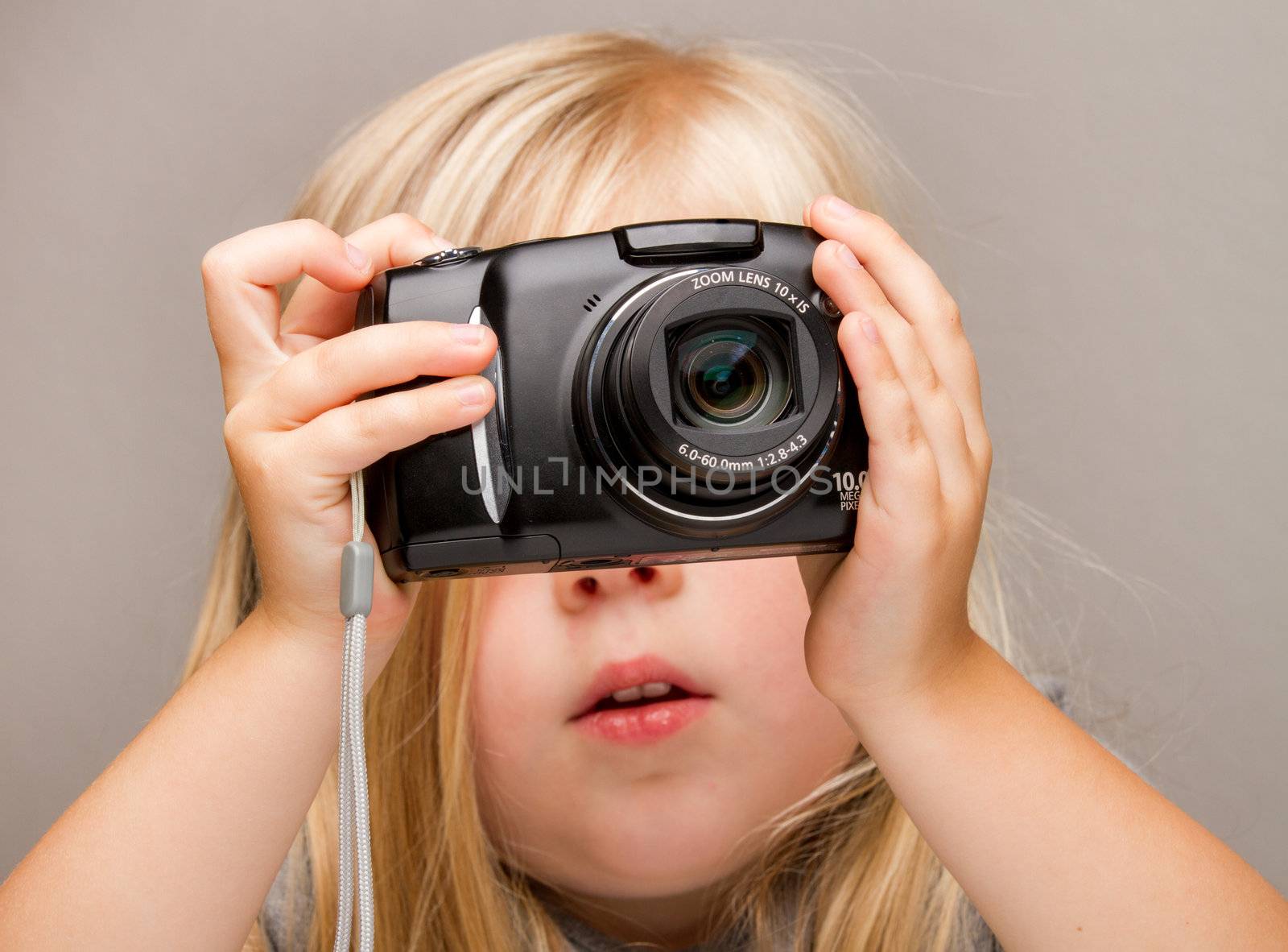 Young child holding a point and shoot camera. Focus is on the camera as she is about to push the button
