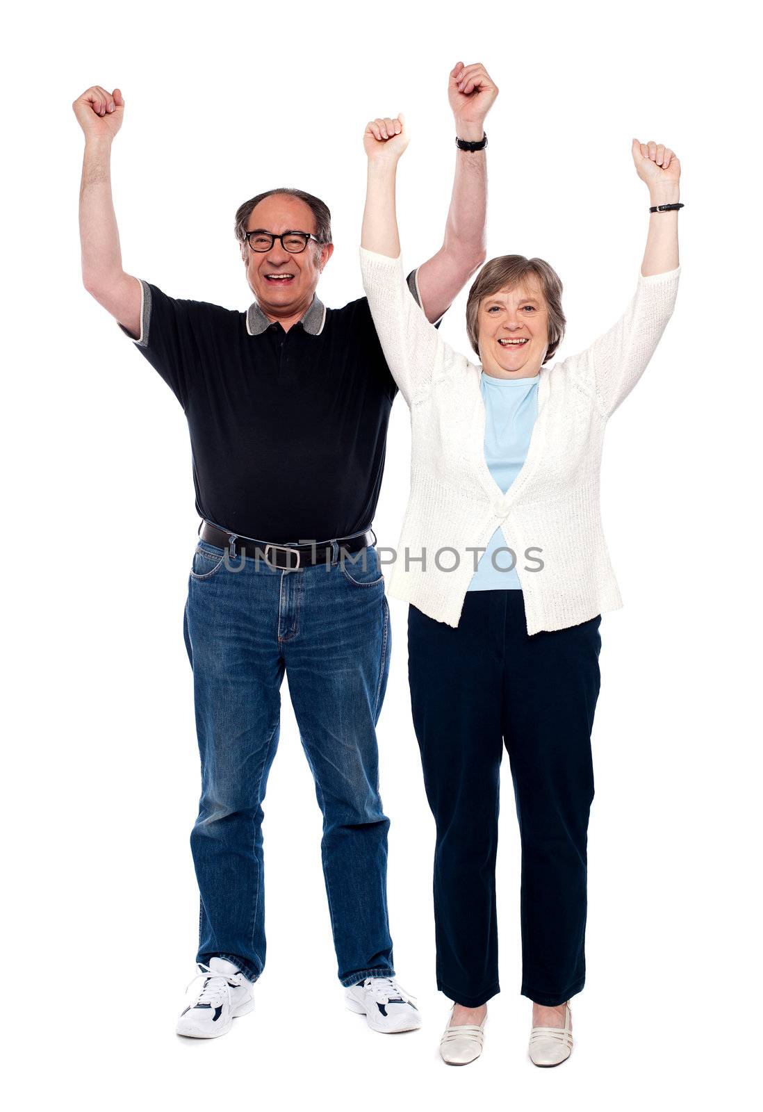 Excited aged couple posing with raised arms by stockyimages