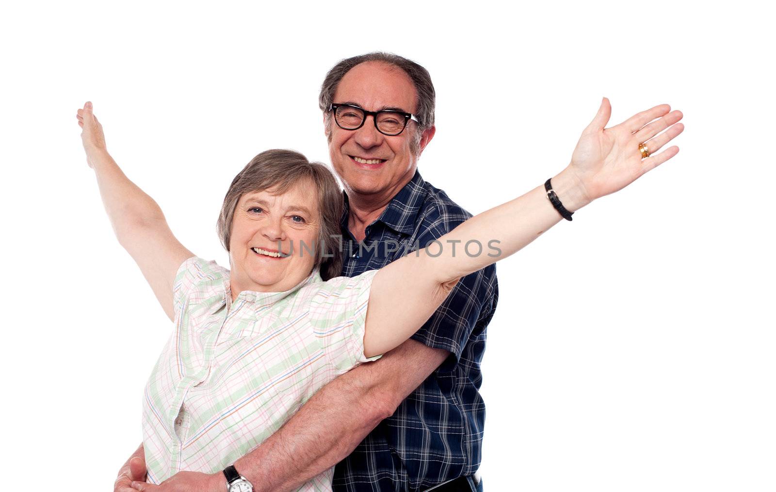 Mature woman with arms outstretched while man hugging her from behind