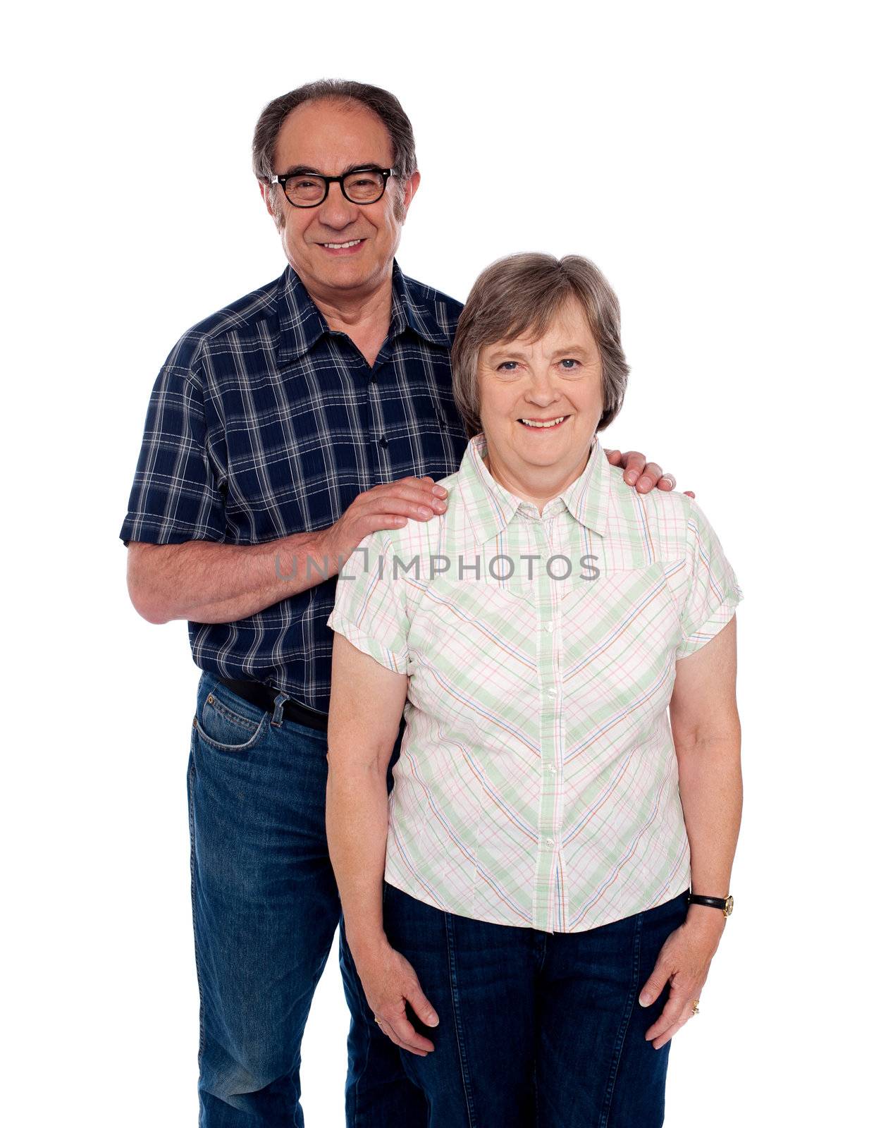 Aged love couple posing with smile. Male resting hands on her woman from behind