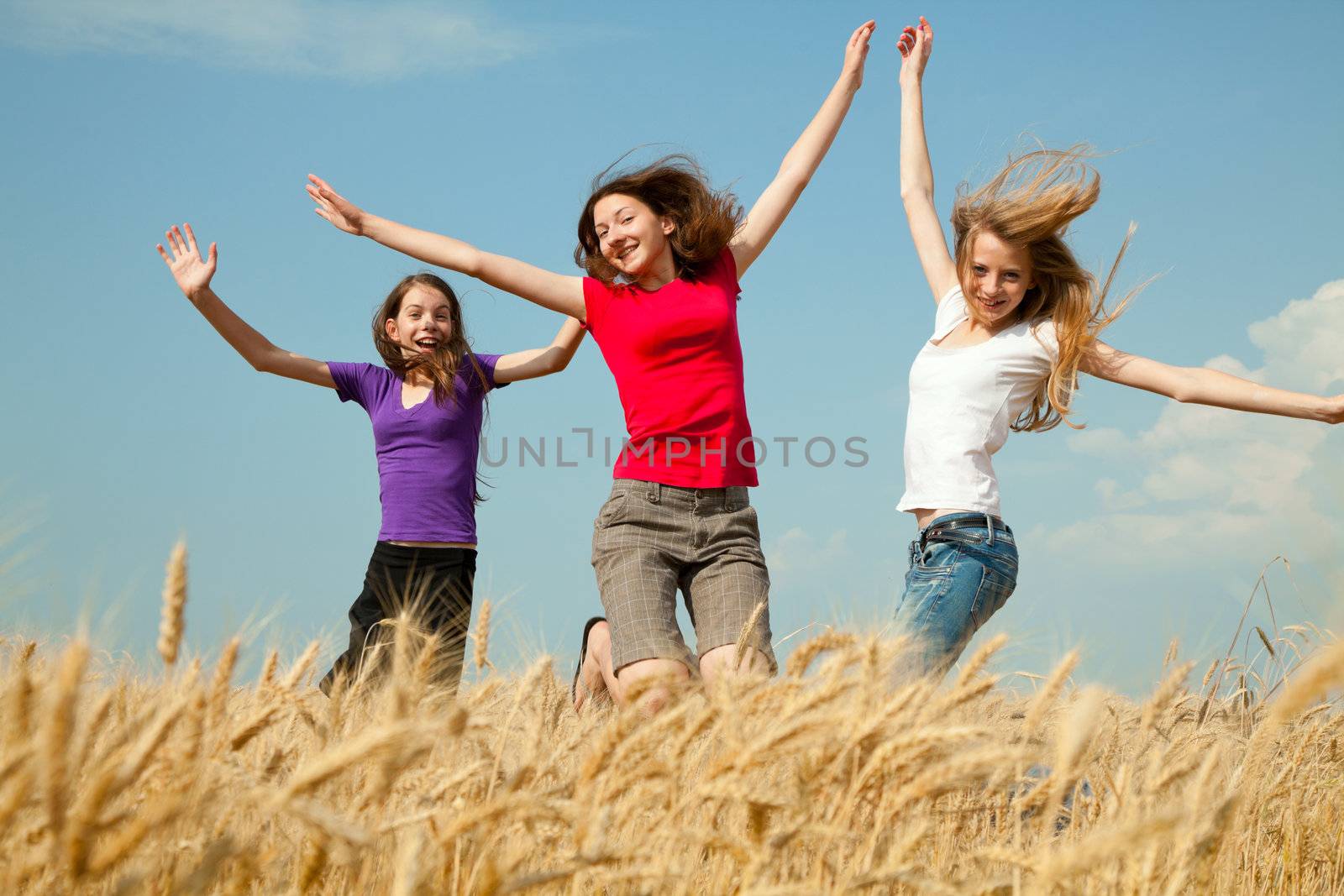 Teen girls jumping at a wheat field in a sunny day