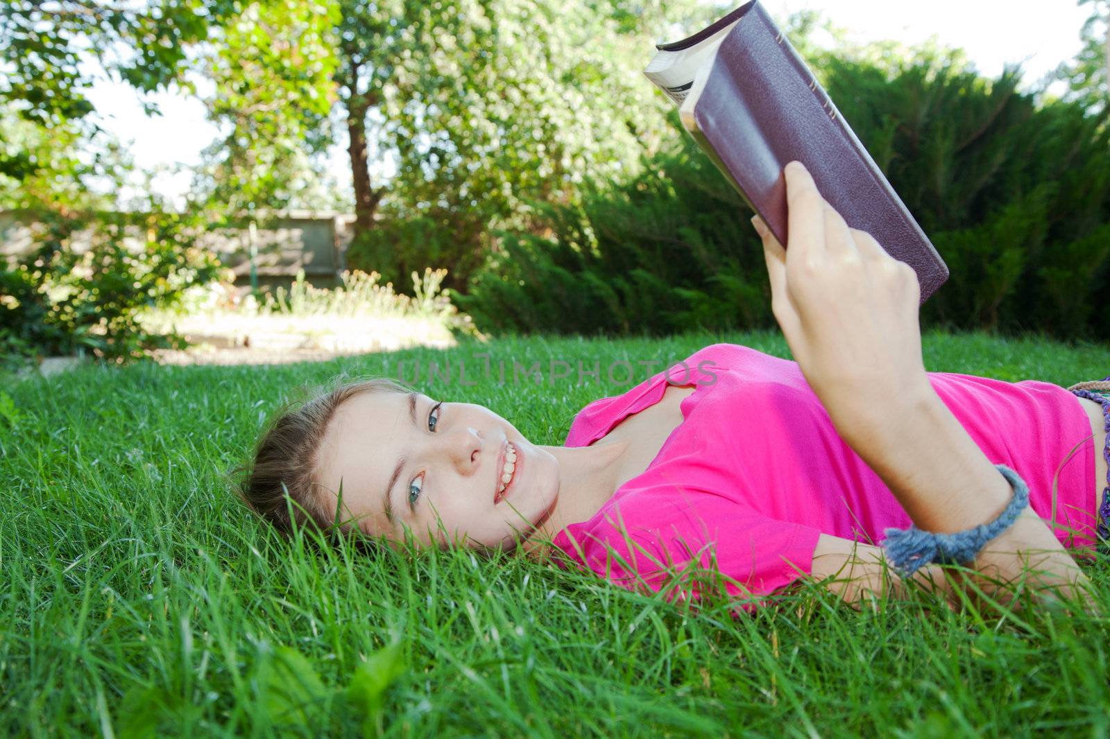 Teen girl reading the Bible outdoors lying on the grass