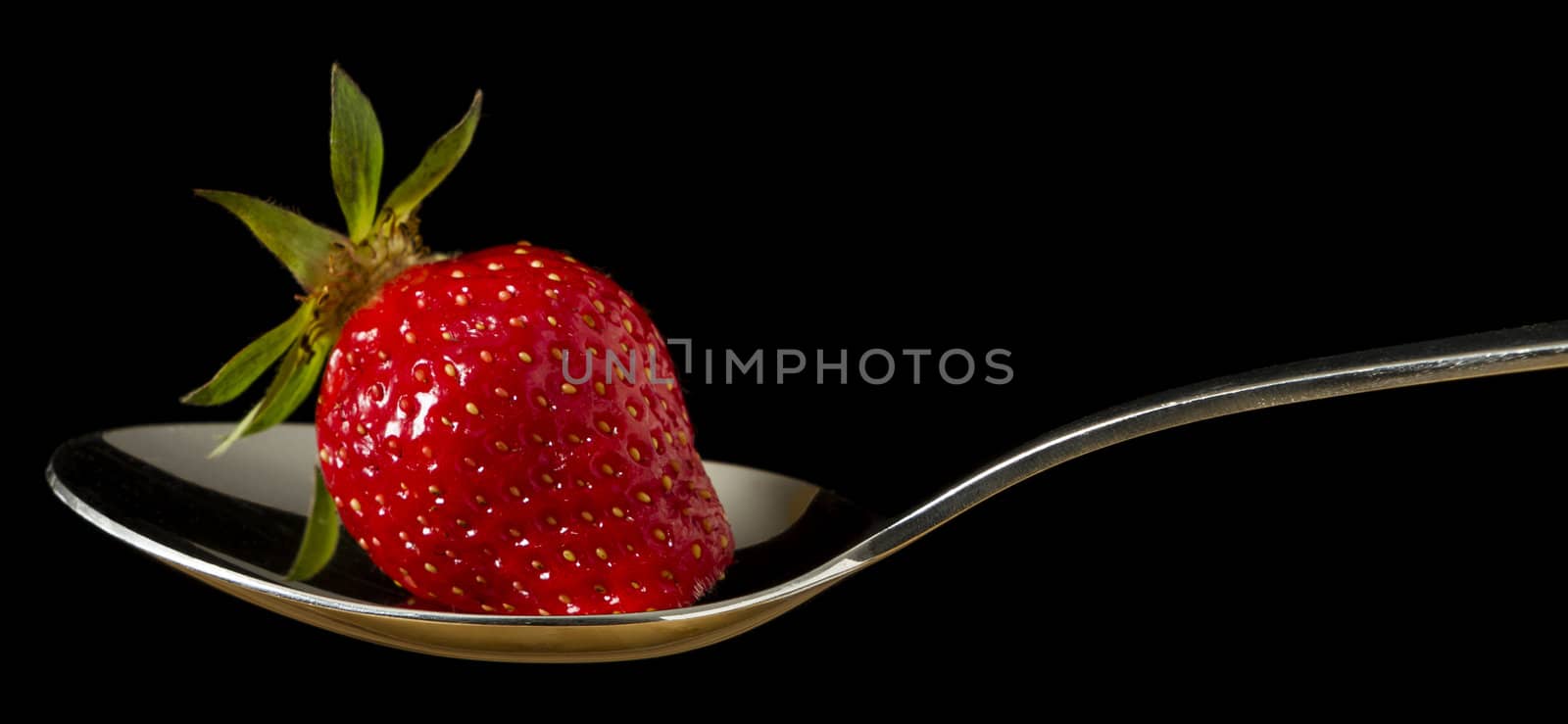 single red, fresh strawberry on spoon in black background