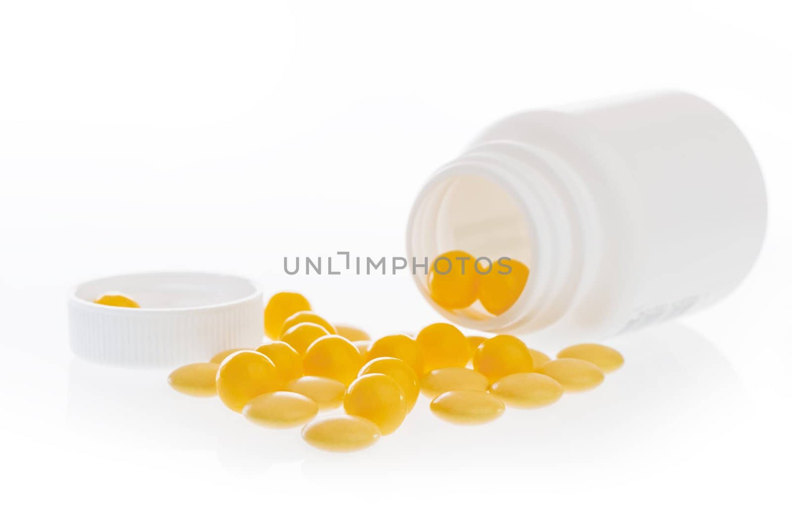 Yellow pills scattered in front of the white plastic jar.