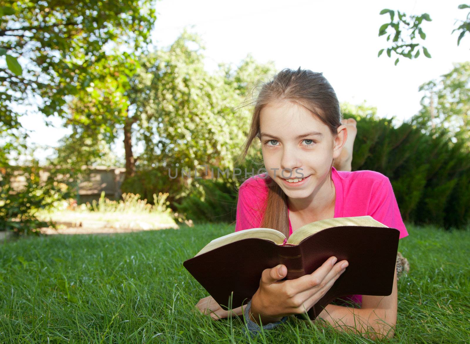 Teen girl reading the Bible outdoors lying on the grass