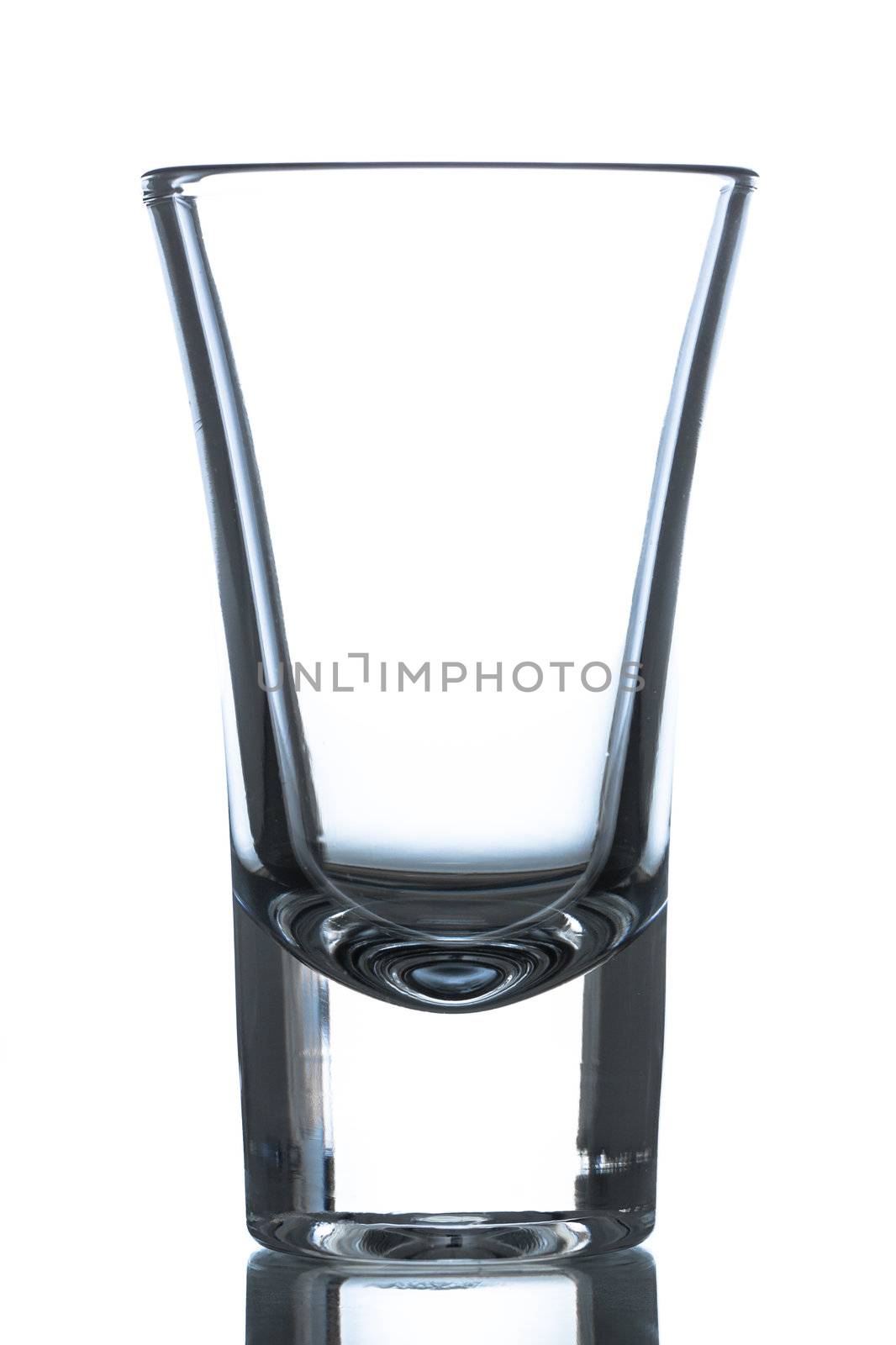 An empty shot glass on a refelctive surface. Isolated on white.