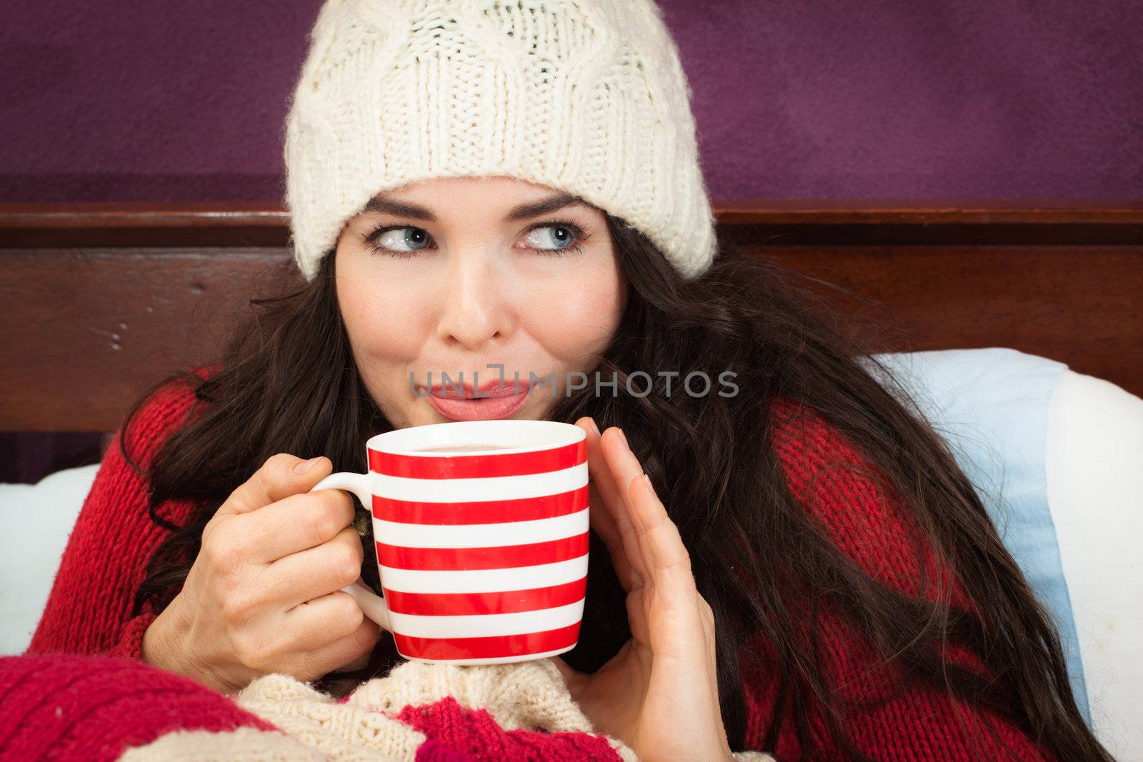 A beautiful young woman enjoying a hot frink under the blankets in bed.