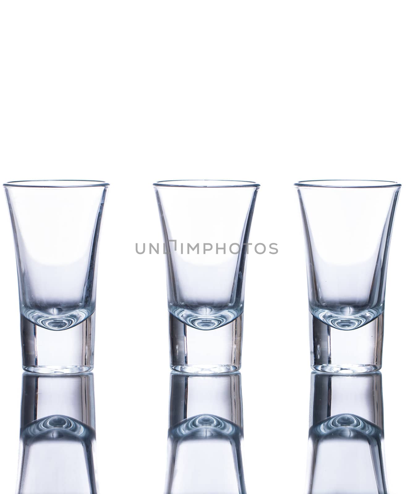 Three empty shot glasses on a reflective surface. Isolated on white.