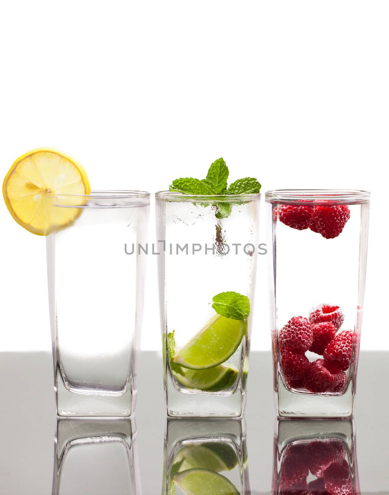 Three colorful alcoholic drinks with various berries, fruit and ice. On a table with reflection and isolated over white.