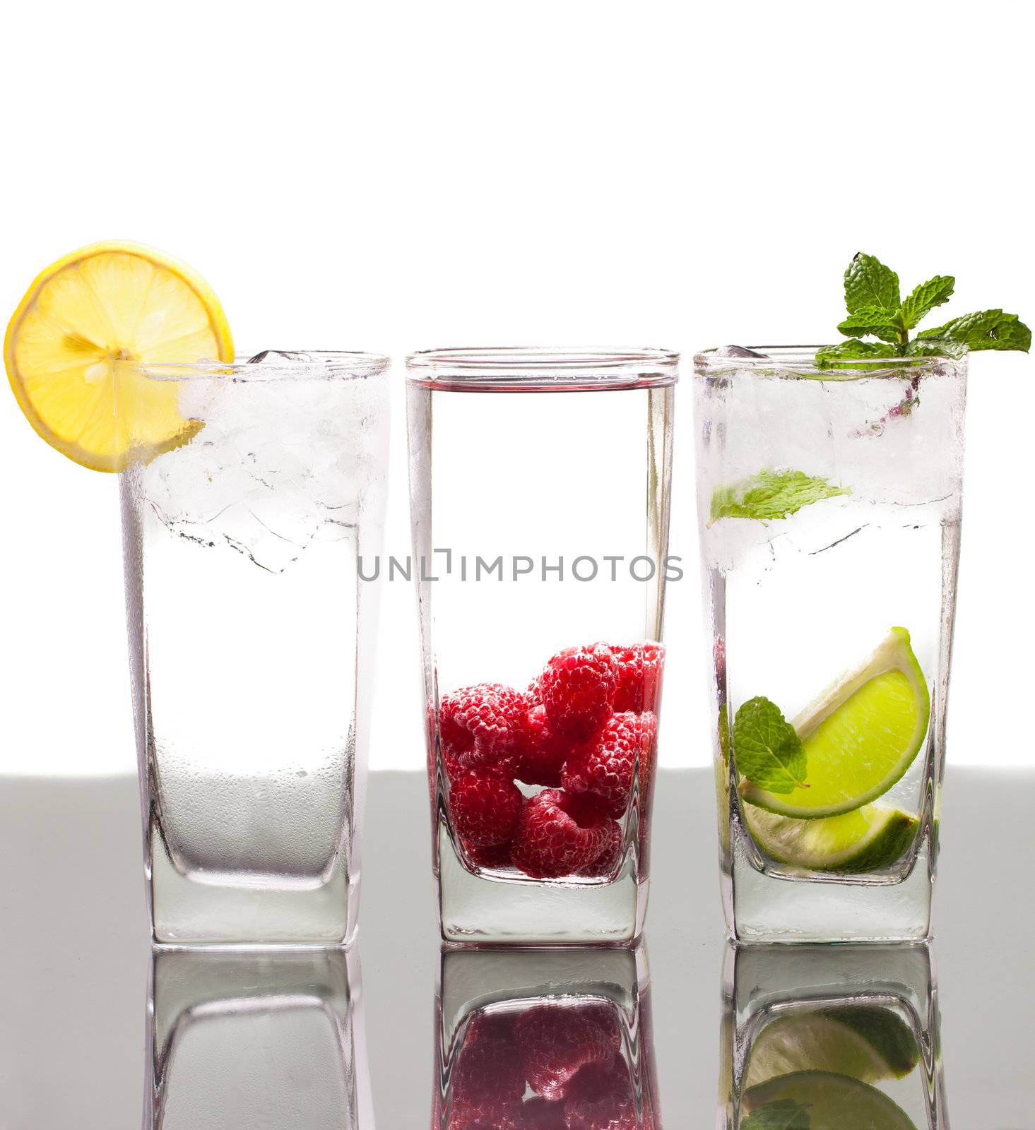 Three colorful alcoholic drinks with berries, fruit and ice. On a table with reflection and isolated over white.