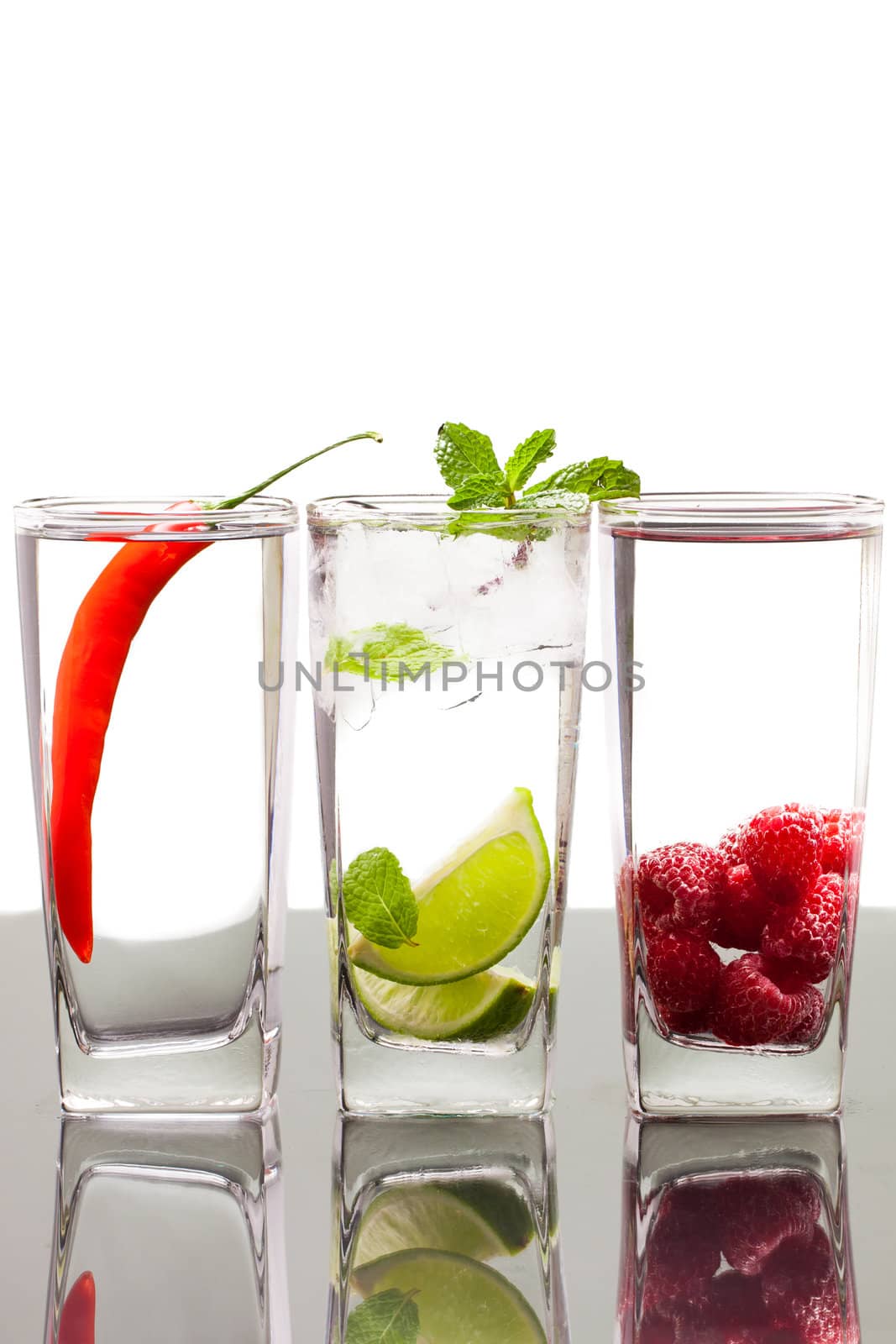 Three glasses with alcoholic drinkswith fruits and berries. On a table with refelction and isolated over white.