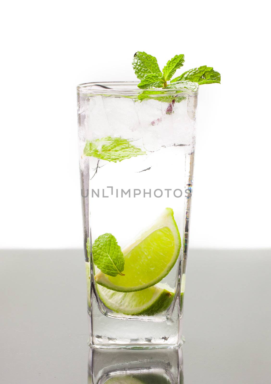 A cold alcoholic drink, mojito, with lime, mint soda and ice. On table with refelction and isolated over white
