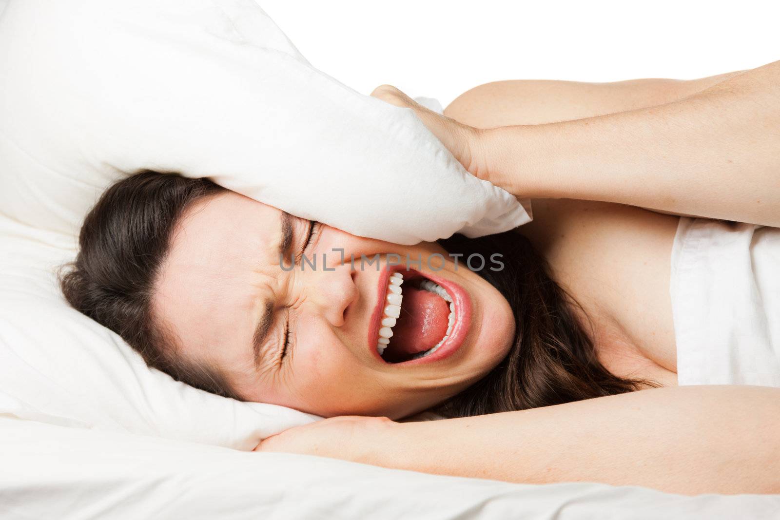 A frustrated tired woman hides her head in her pillow and screams beacuse she can't sleep. Isolated on white.