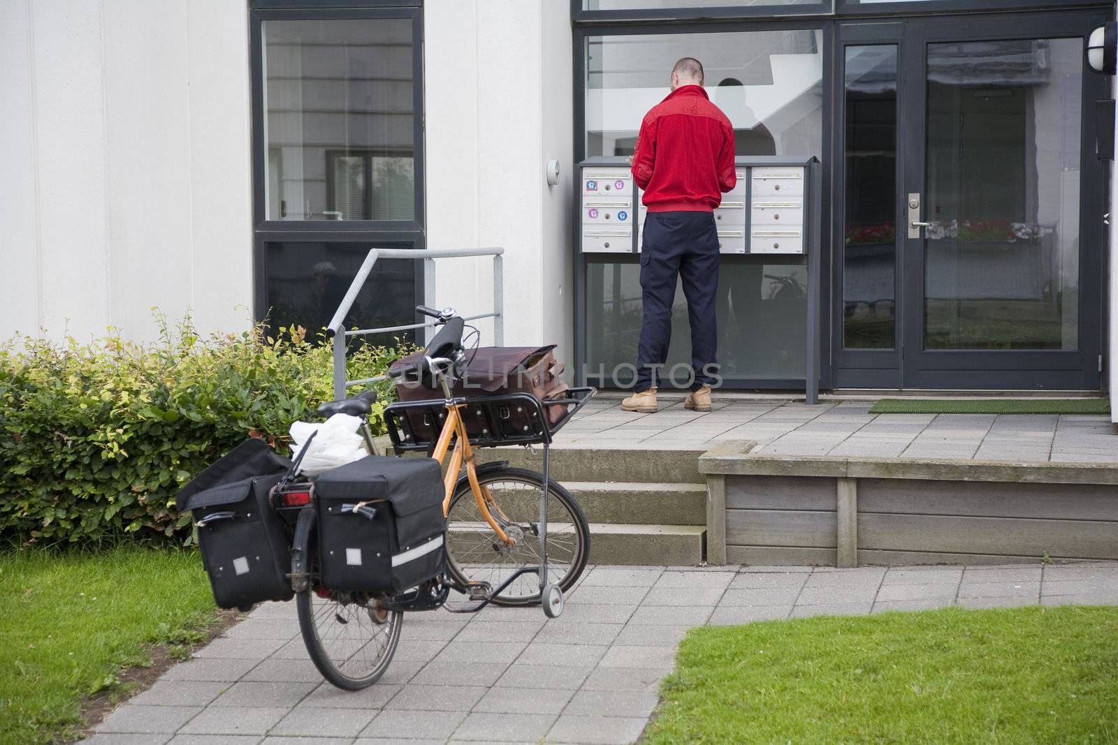 Danish postman distributing letters in a waterfront condominium  at summertime in Nyborg, Denmark.