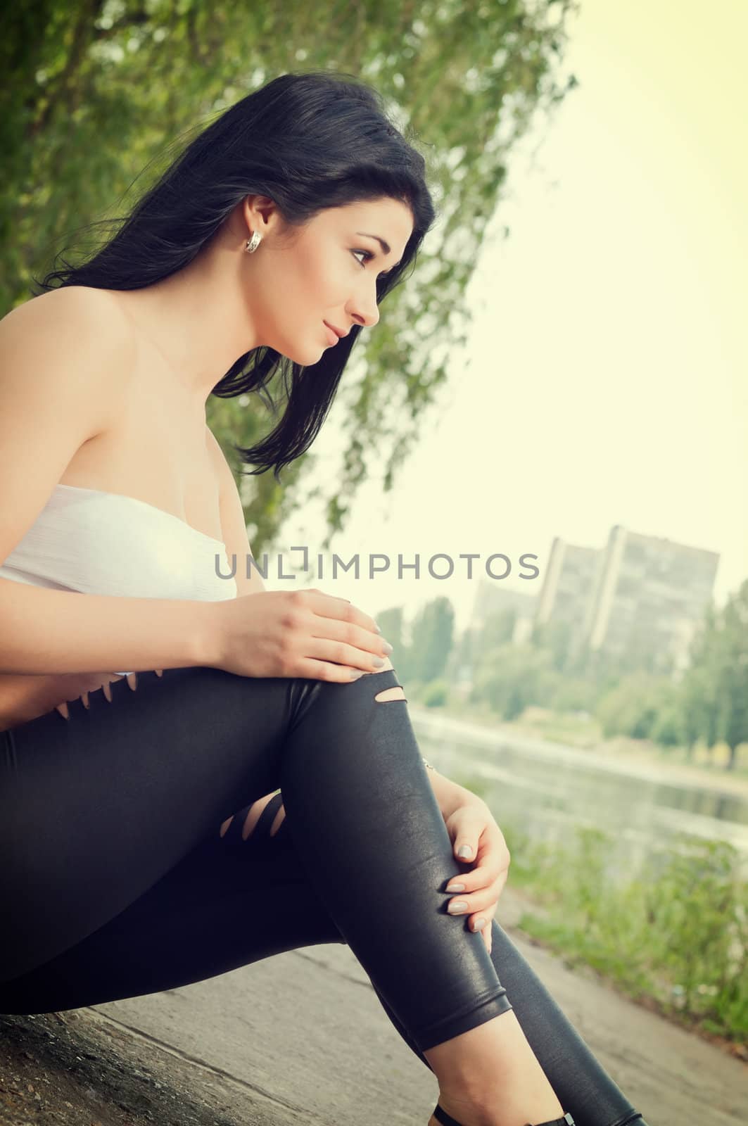 Girl sits on banks of city pond.