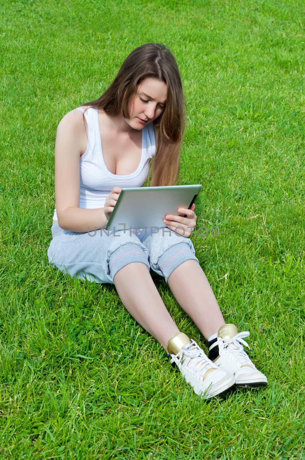 Girl working intently tablet sitting on grass in park.