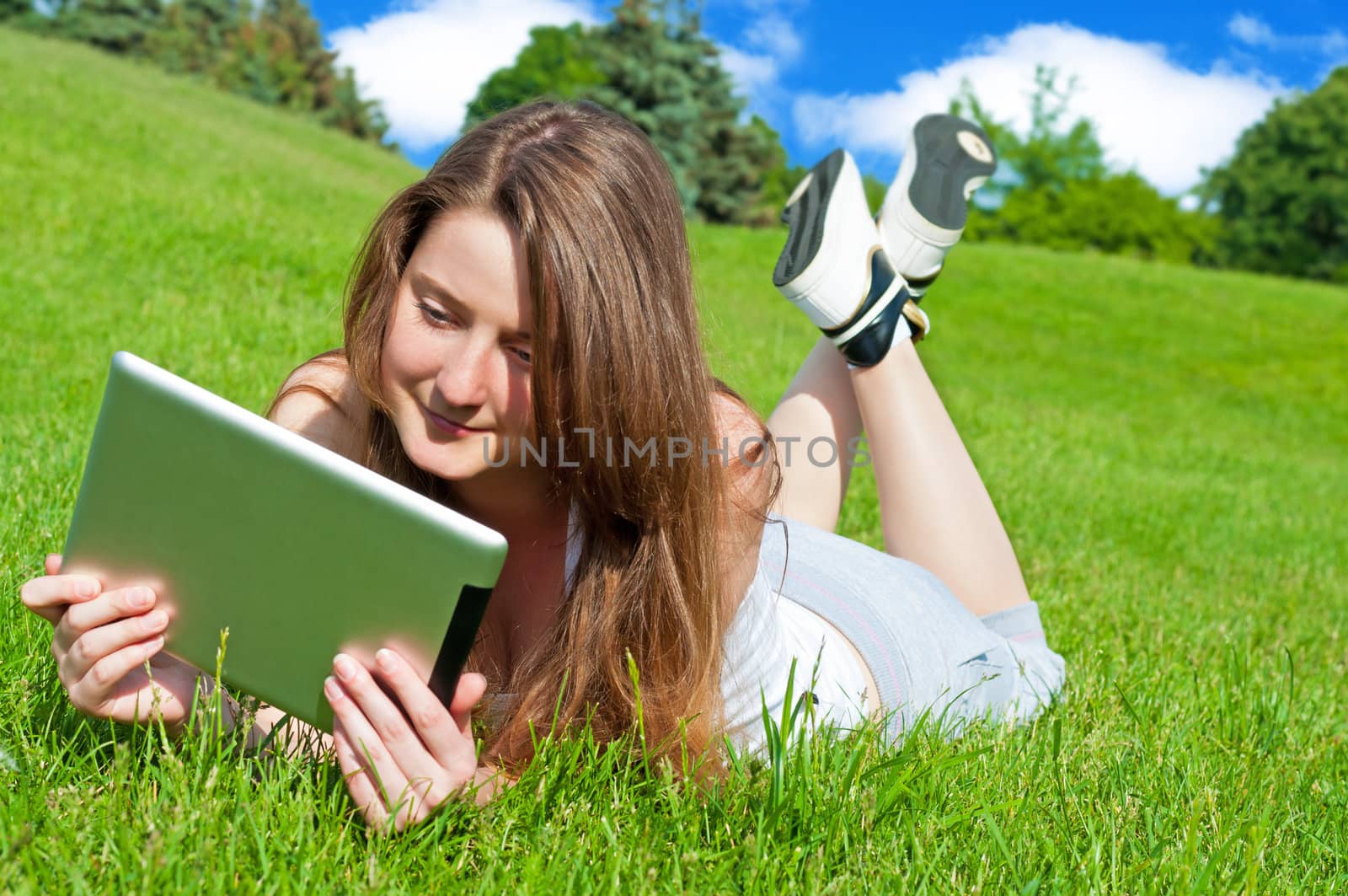 Pretty girl with tablet lying on grass in park.