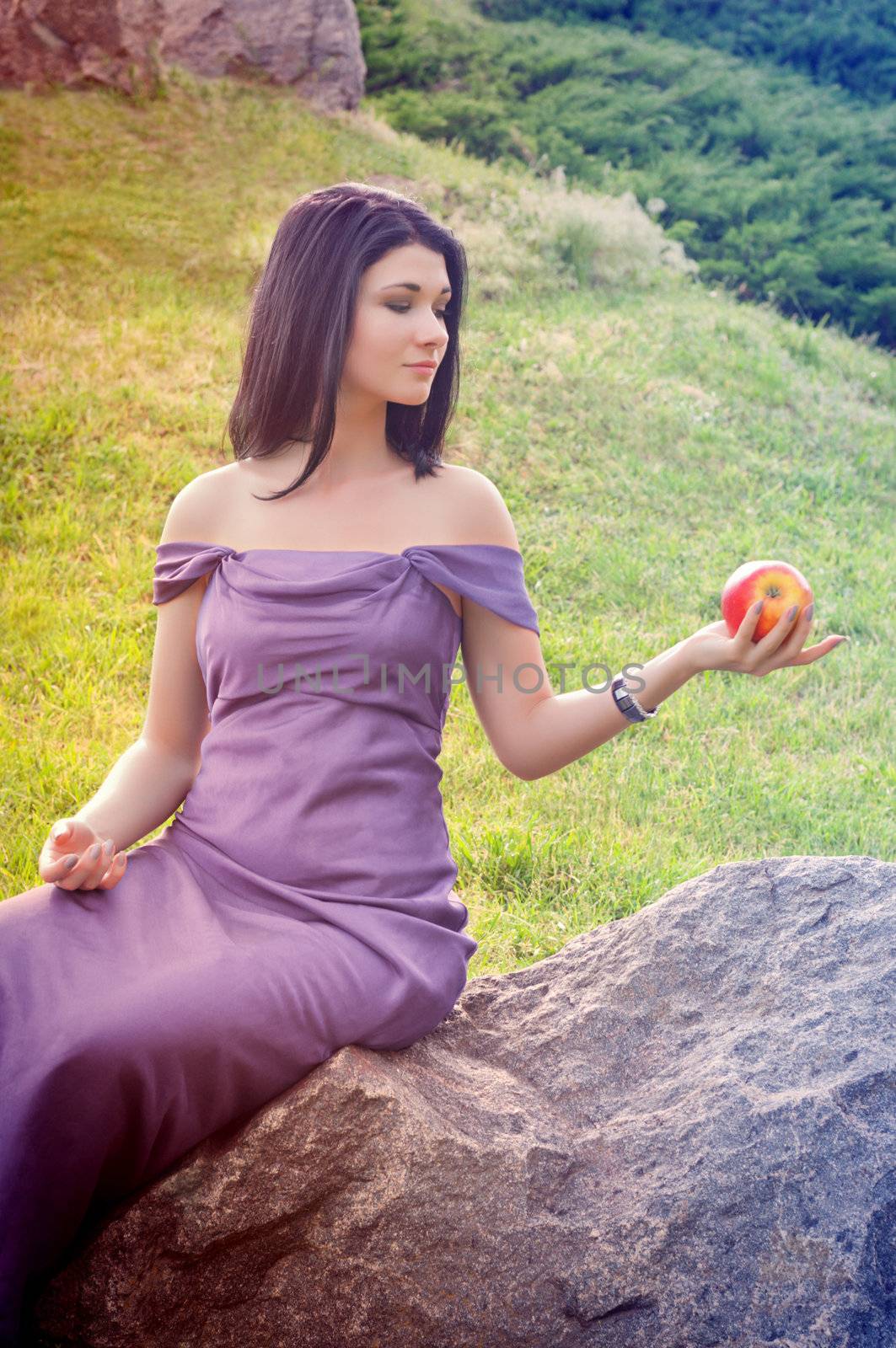 Girl is sitting on rock and looking at apple in his hand that holds.
