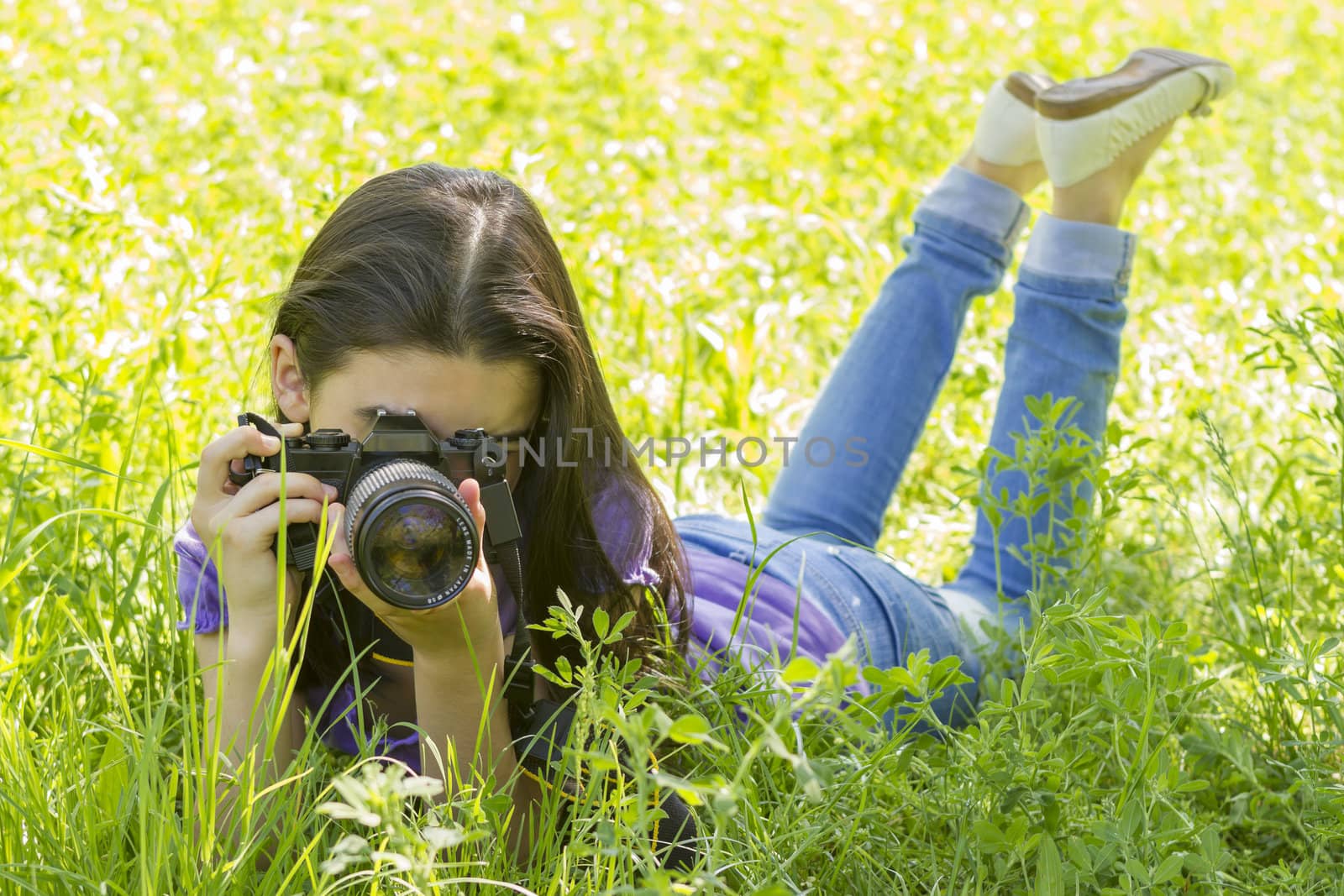 Young girl laying on grass and making photos at summer green park.