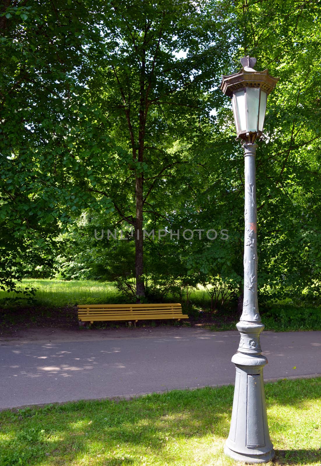 Vintage retro park lamp light pole and yellow wooden bench under trees for recreation.