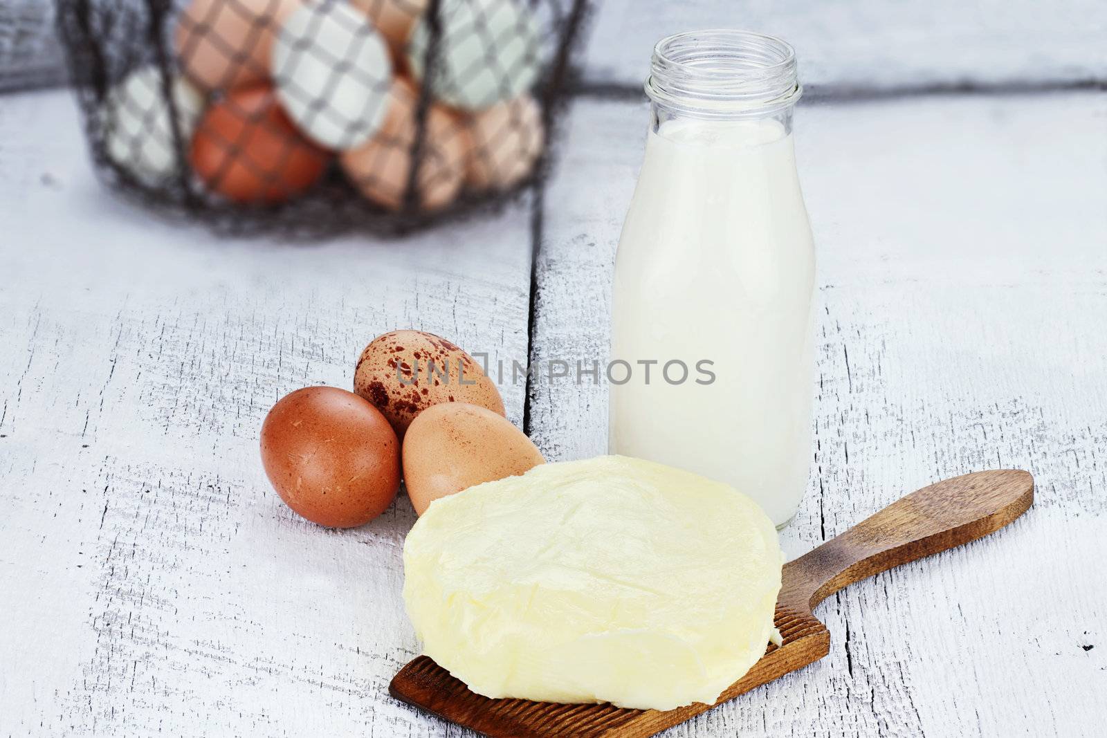 Farm fresh milk, butter, and eggs against a rustic background. Milk is in a vintage glass milk bottle. Shallow depth of field. 