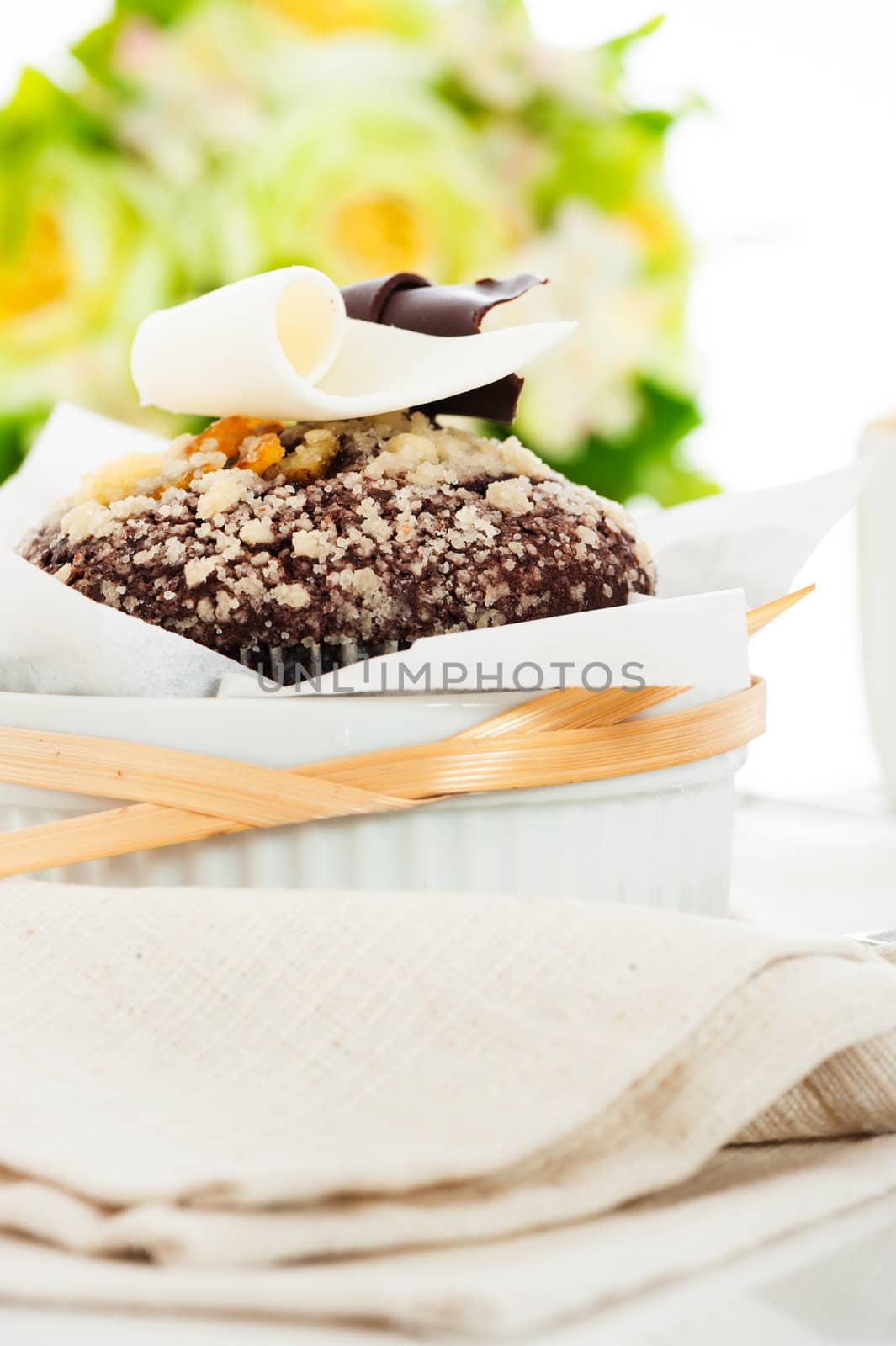 Chocolate muffin with white and dark chocolate on the top and flower as decoration in the background