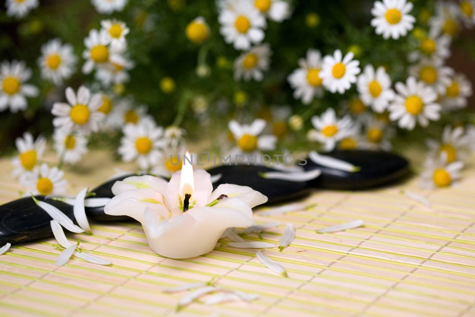 A burning candle and black stones for spa massage