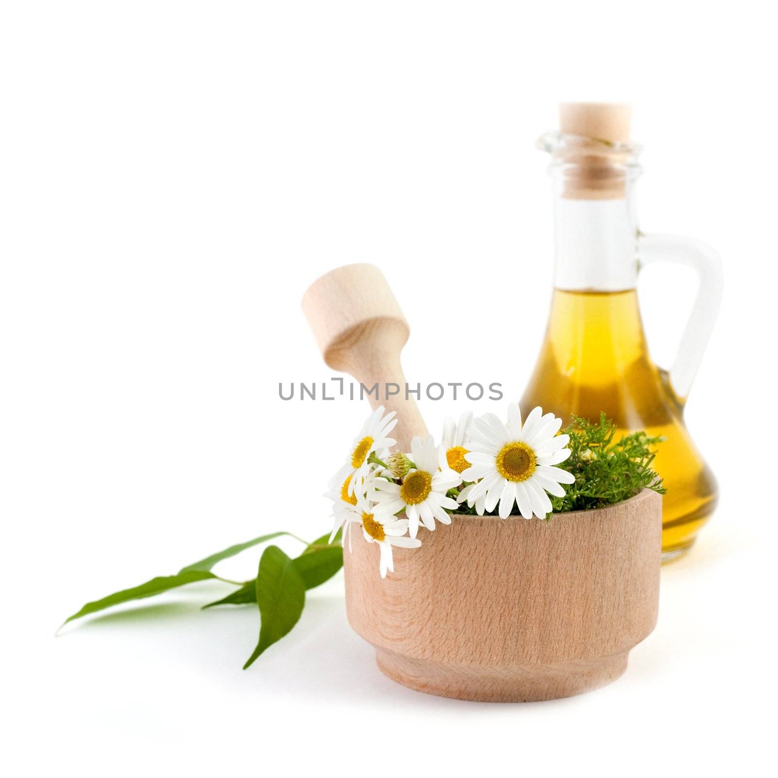 A wooden mortar with flowers in it and a bottle of oil
