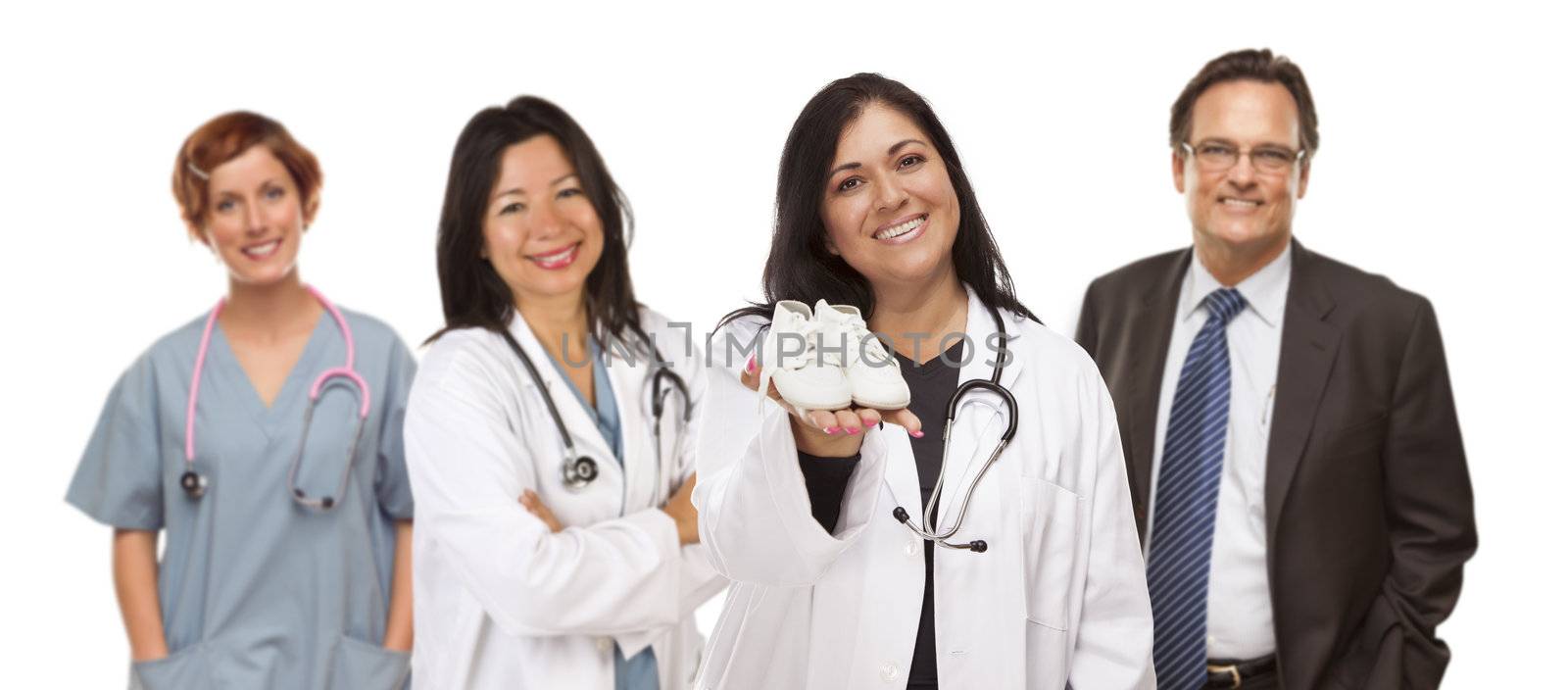 Attractive Hispanic Female Doctor or Nurse Holding Out Baby Shoes and Support Staff Behind Isolated on a White Background.