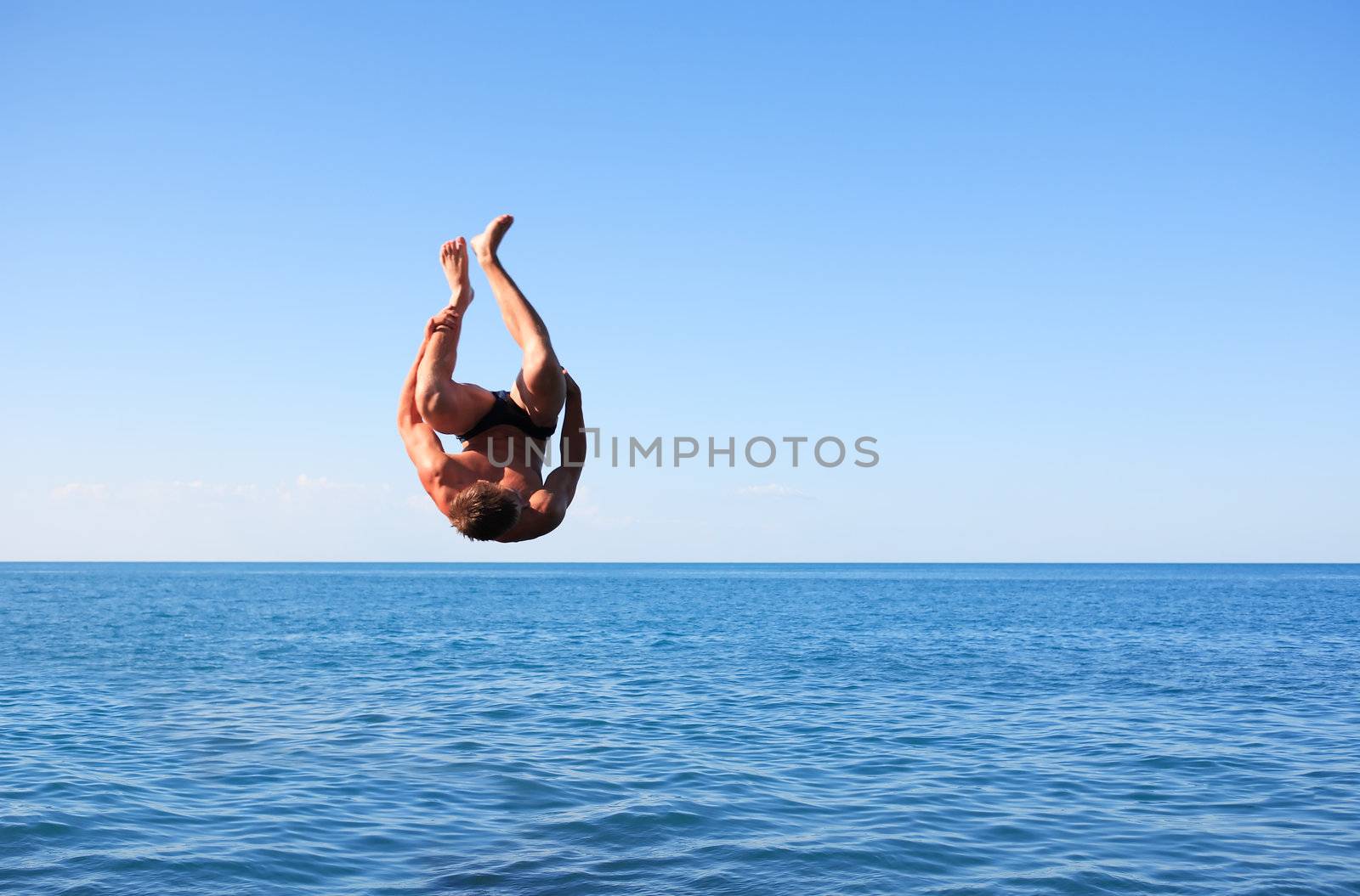 Young strong man doing somersault between blue sky and sea