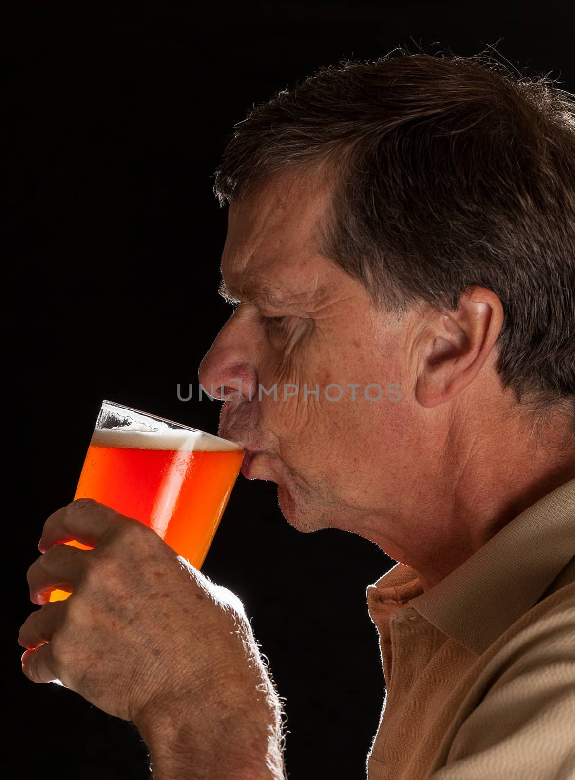 Senior caucasian man in profile drinking from a pint glass of beer or lager